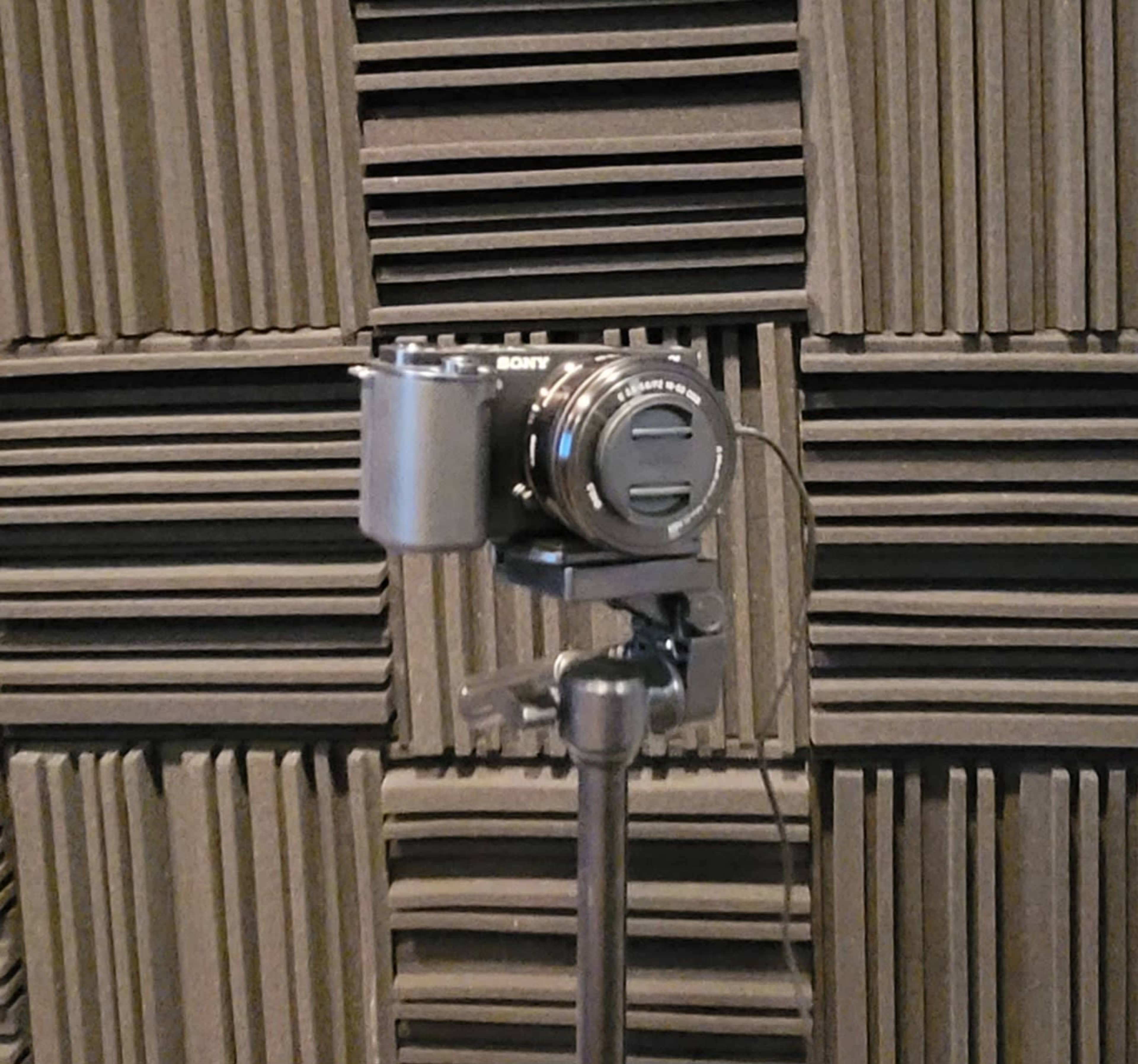 A camera is mounted on a tripod in front of a wall covered in acoustic foam panels.