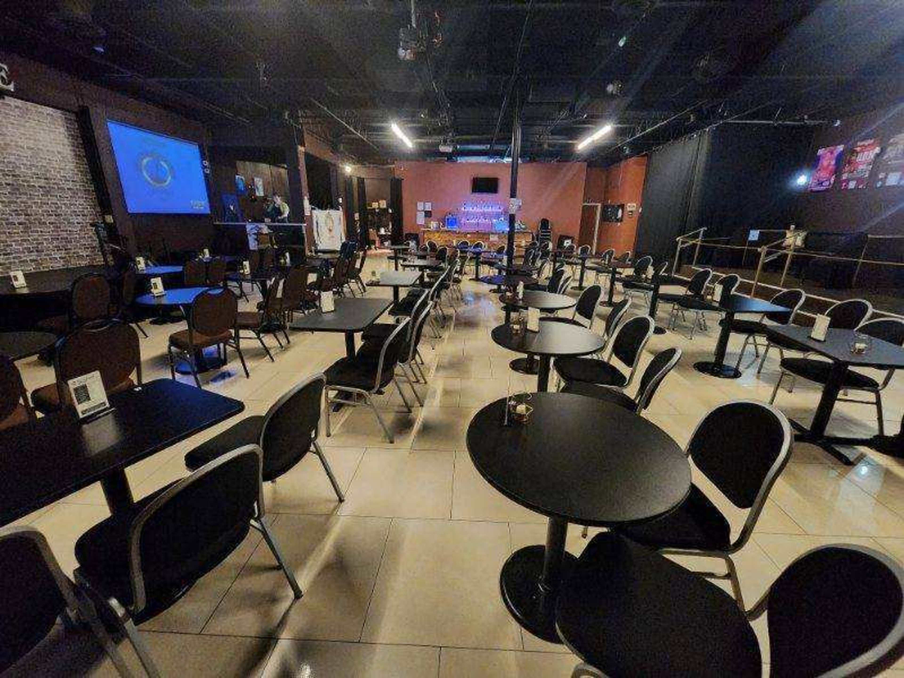 An empty indoor venue with rows of round tables and chairs arranged for an event, accompanied by a stage at the front.