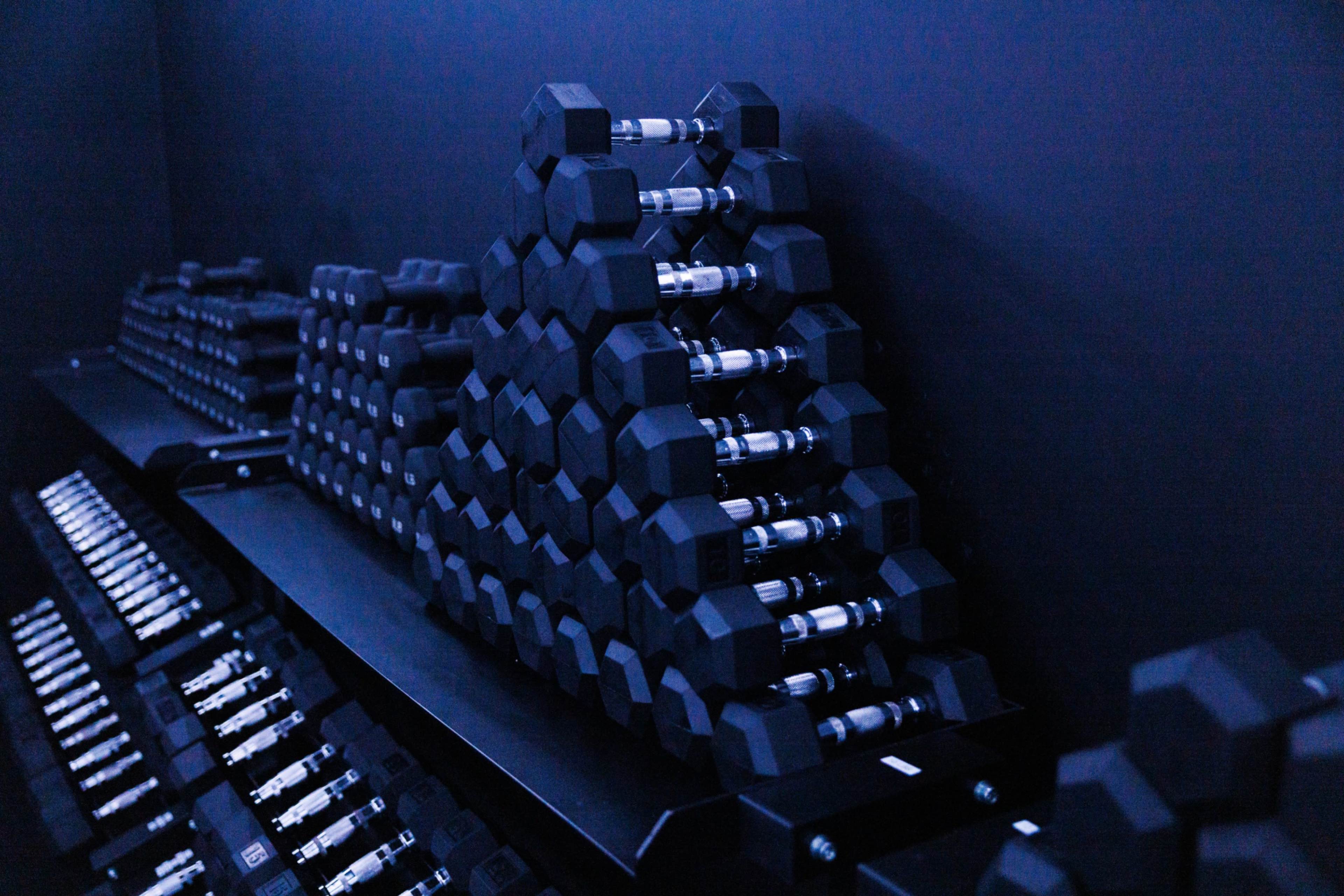 The image shows a neatly organized rack of hexagonal dumbbells arranged in a pyramid formation against a dark background.