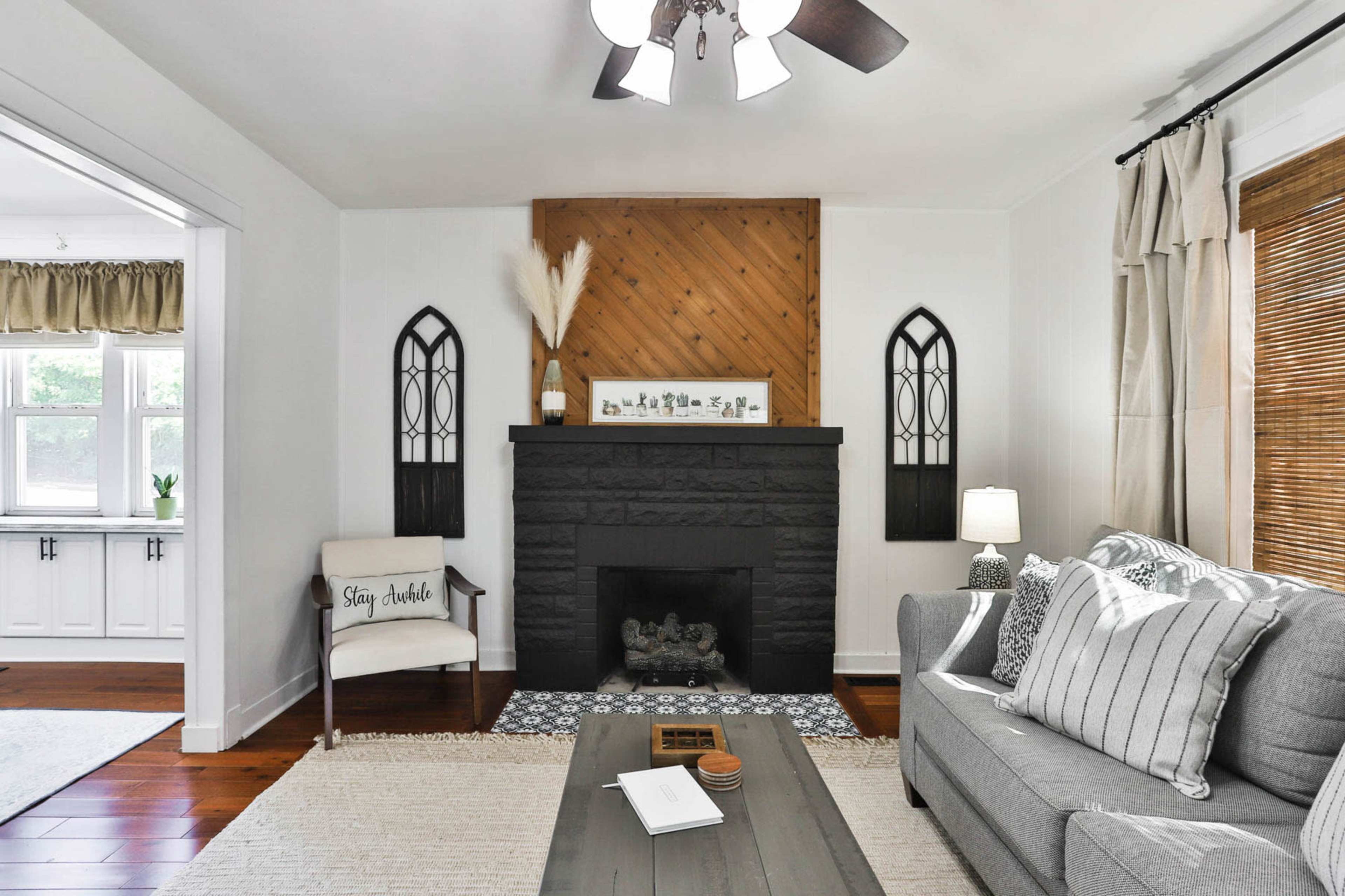 A living room with a gray sofa, a black stone fireplace, wooden accents, and decorative wall frames.