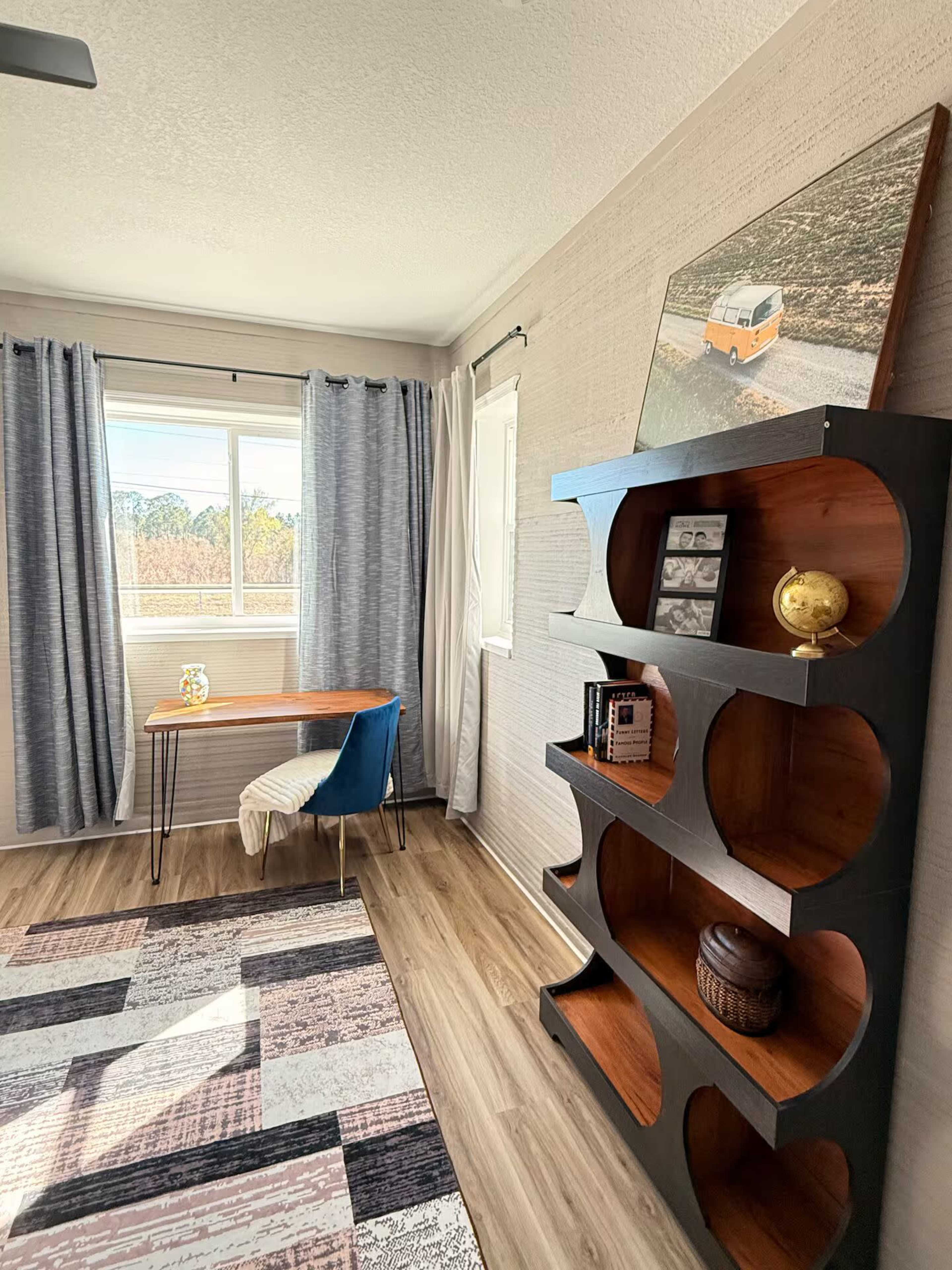 The image shows a bright room featuring a wooden desk by a window, a bookshelf with circular cutouts, and textured gray curtains.