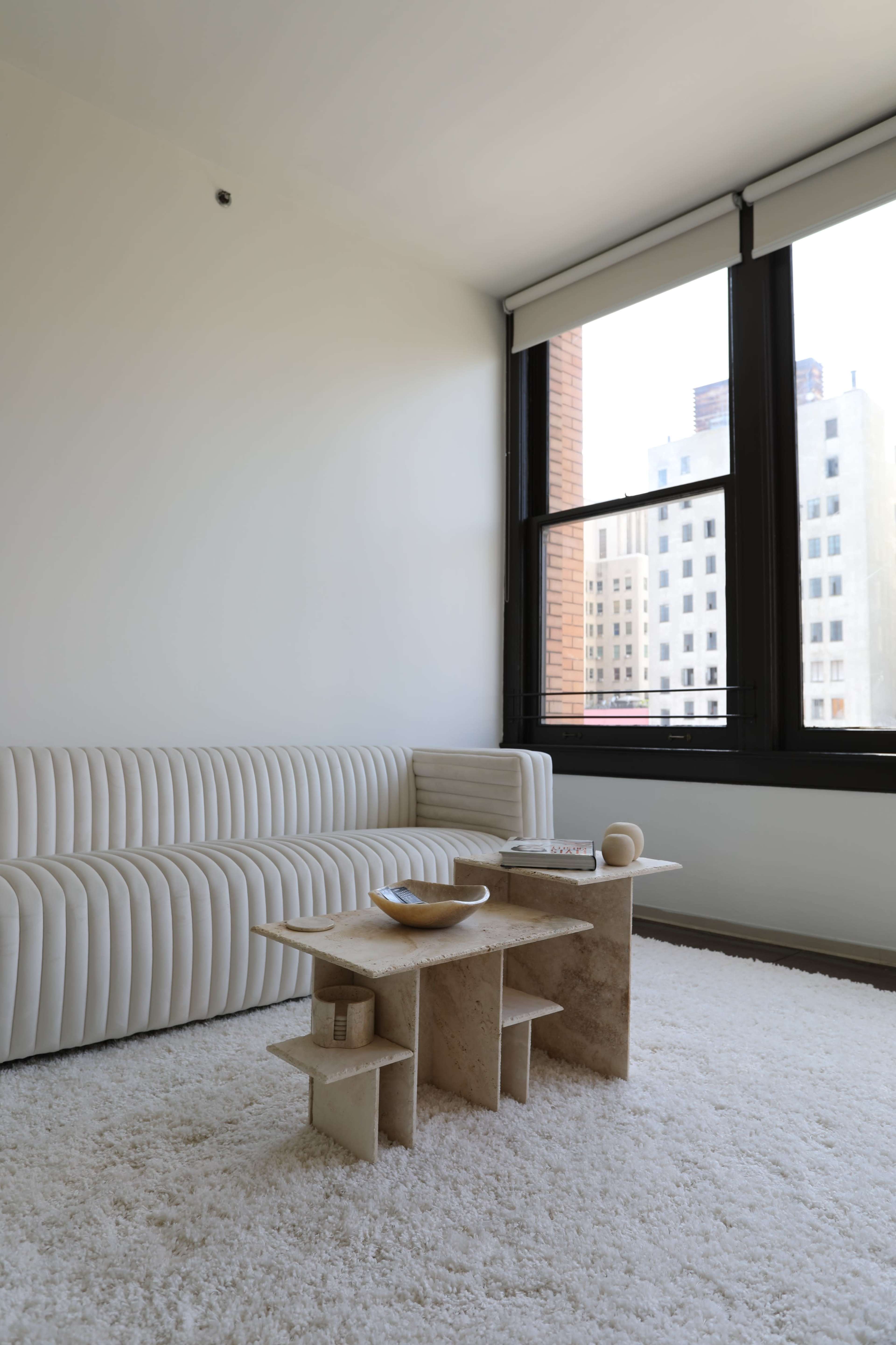 A modern living room with a ribbed white sofa, a minimalist stone coffee table, and large windows overlooking a cityscape.