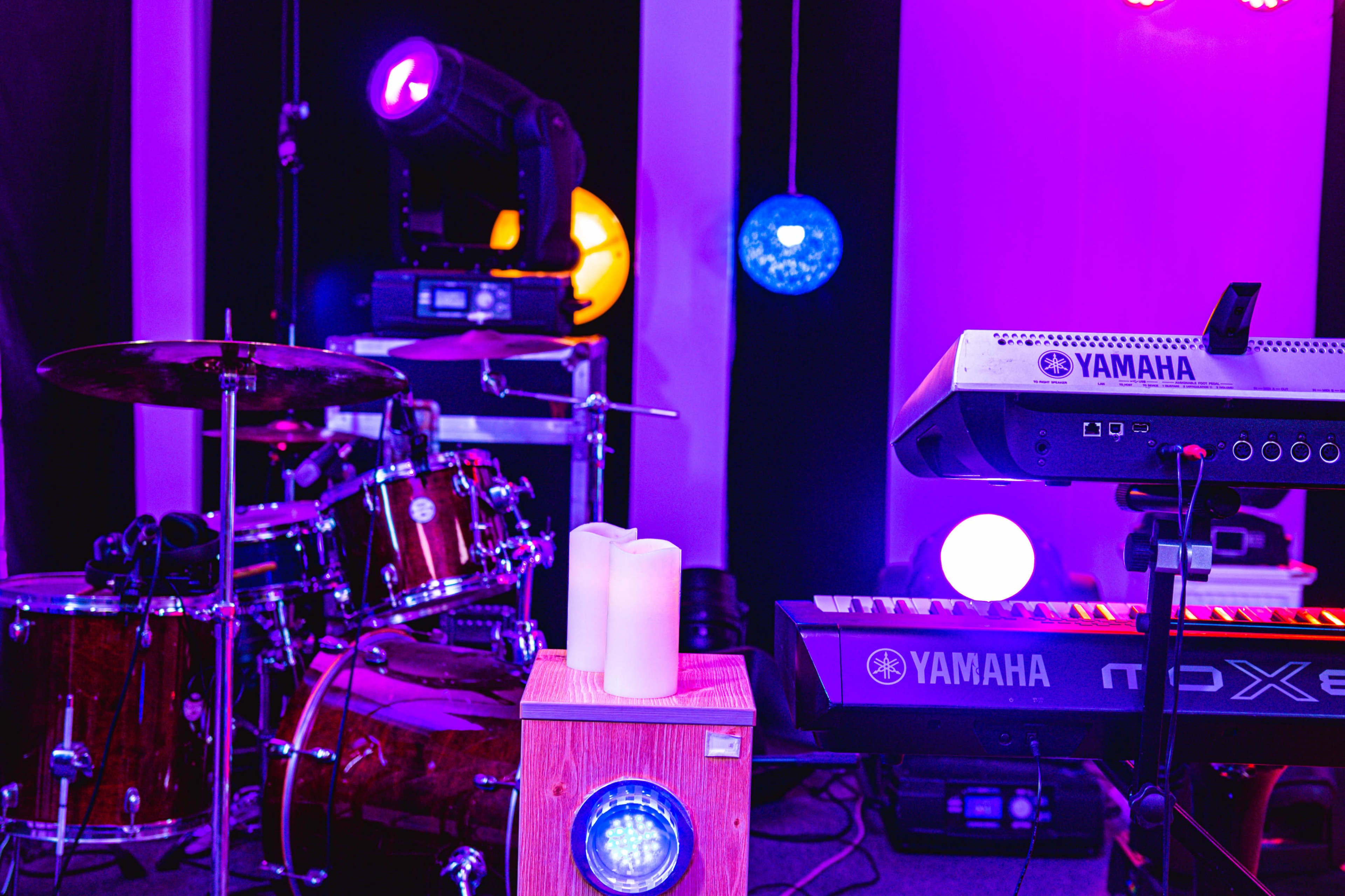 A music setup featuring a drum kit, a keyboard, and various lighting elements in a well-lit studio environment.