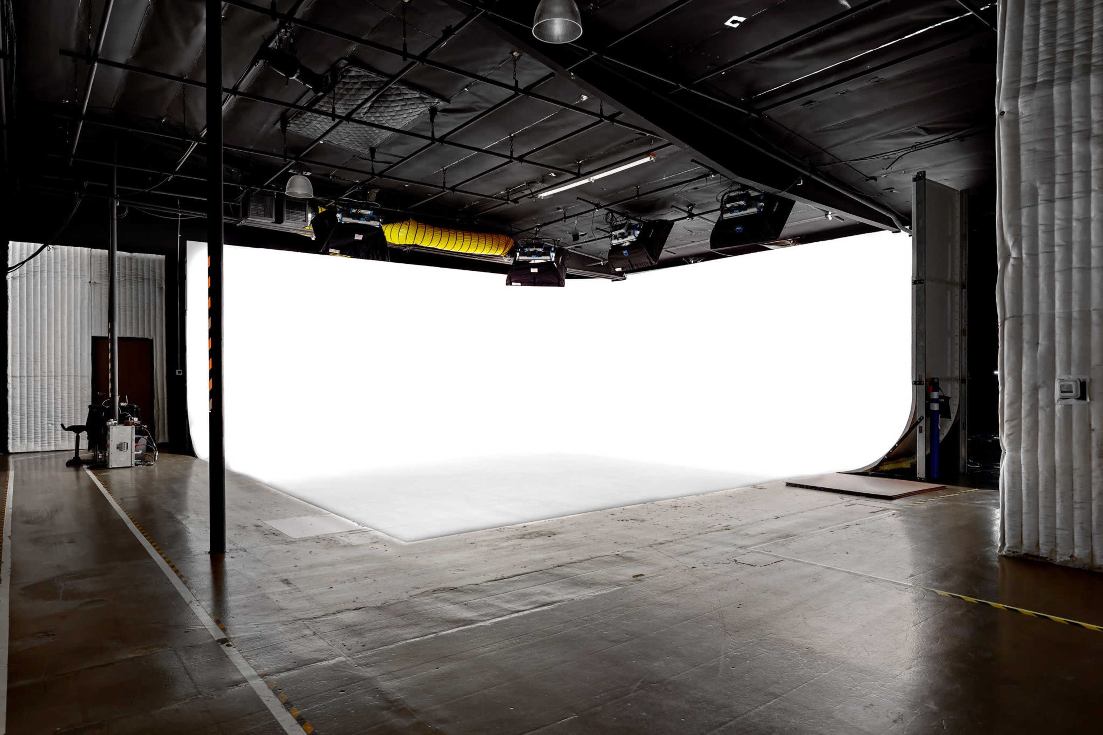 The image shows a spacious studio with a large white backdrop and overhead lighting equipment.