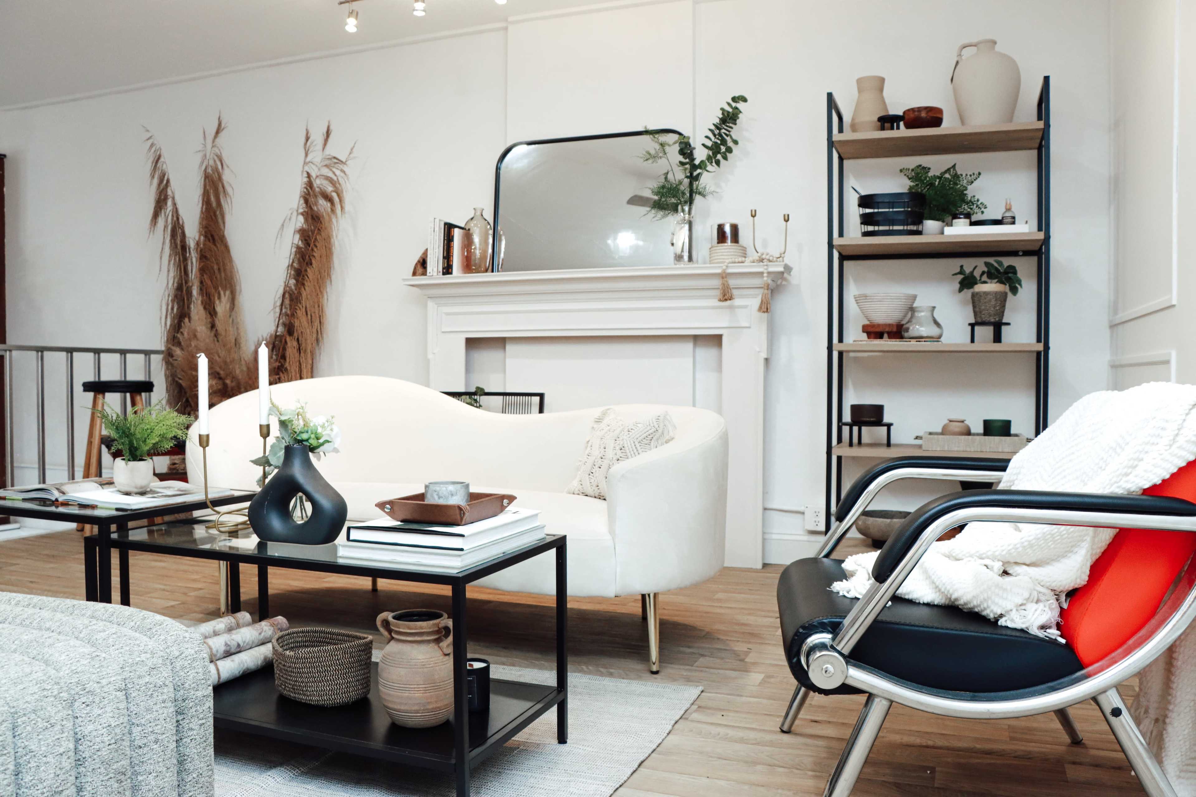 A modern living room featuring a white curved sofa, a black and red chair, a coffee table with decorative items, and a fireplace with a mirror above it.
