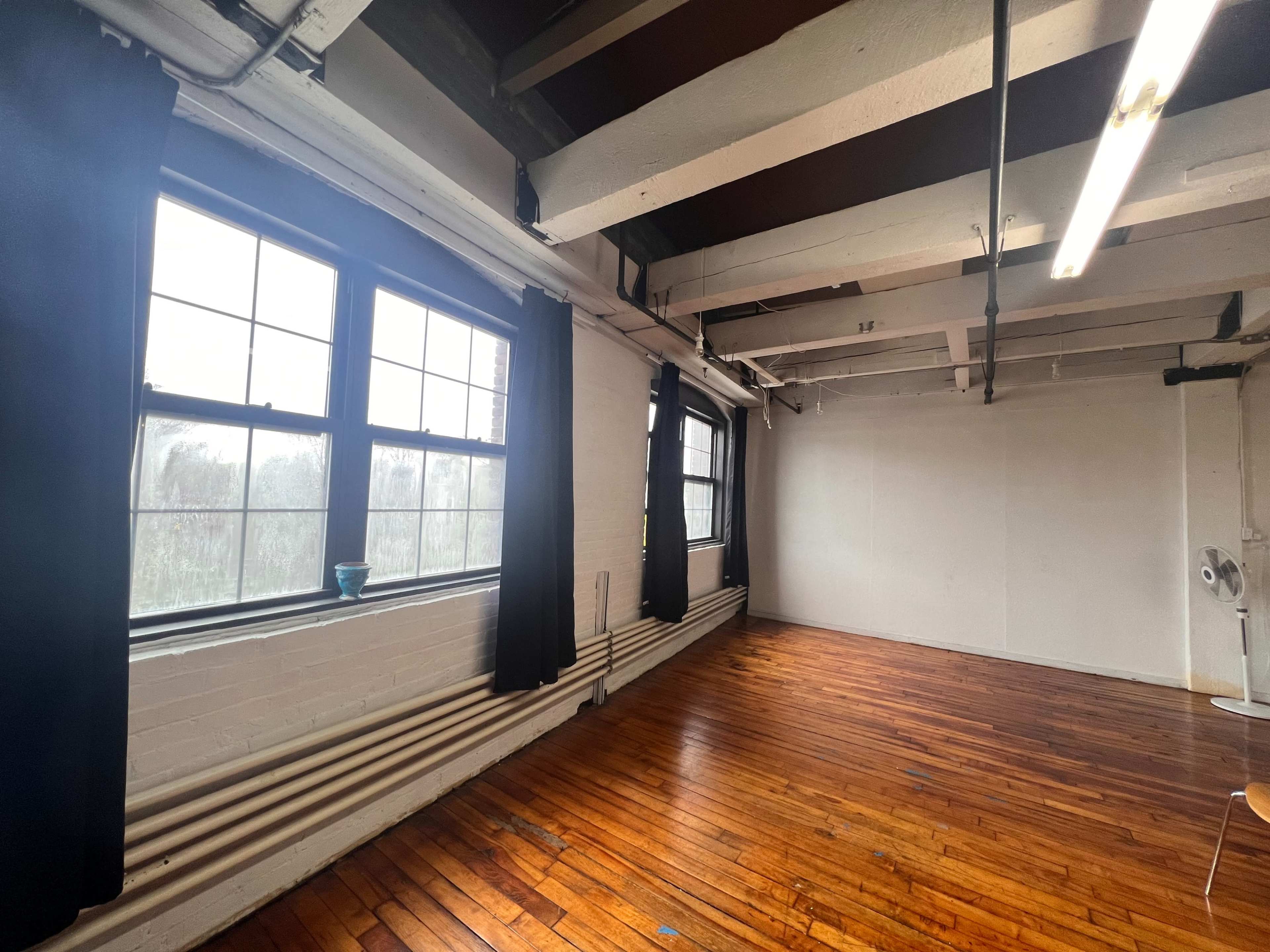 The room features large windows with black curtains, wooden flooring, and exposed beams on the ceiling.