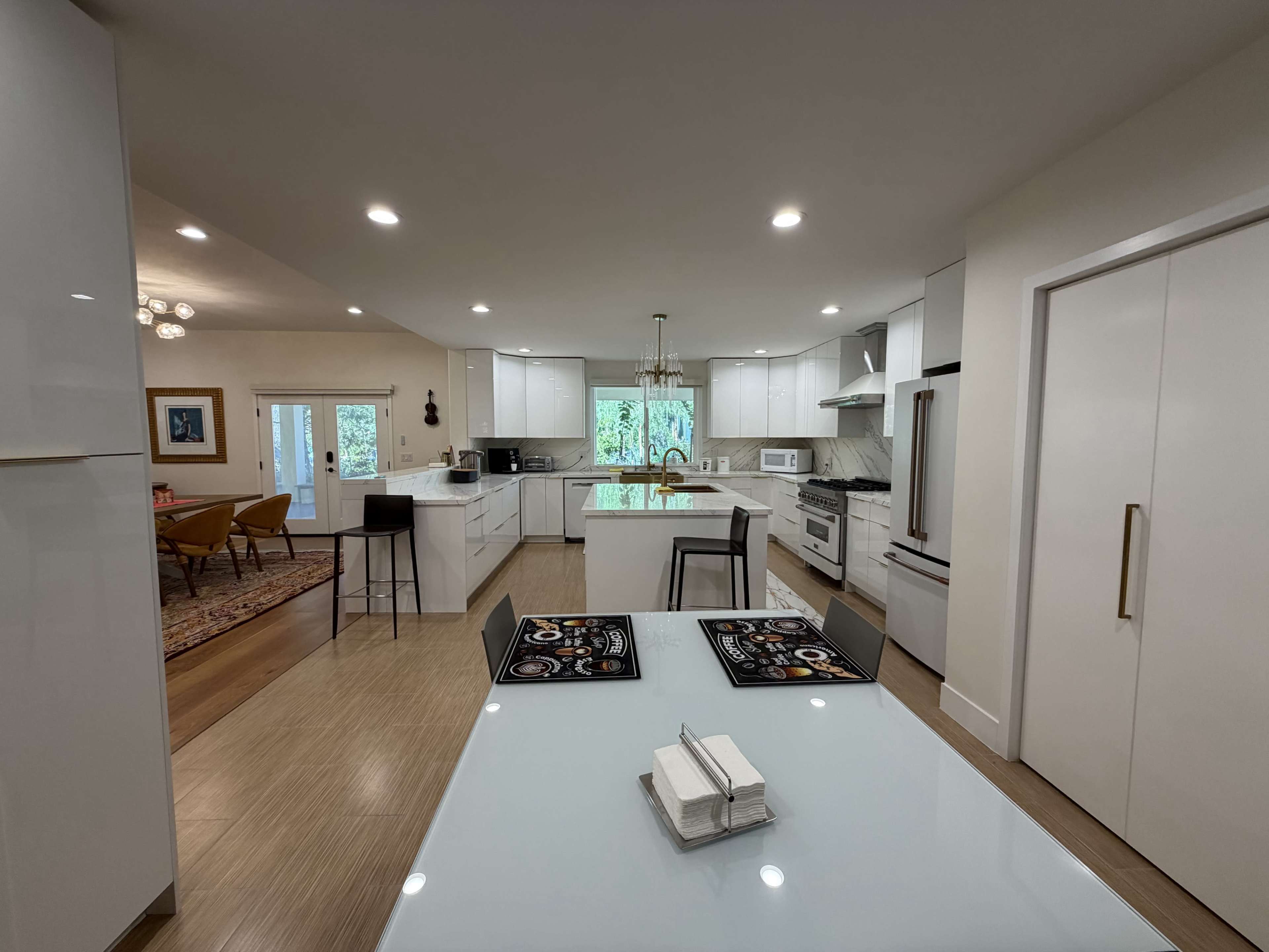 The image shows a modern kitchen with white cabinetry, a central island, and an adjoining dining area in a bright, open layout.