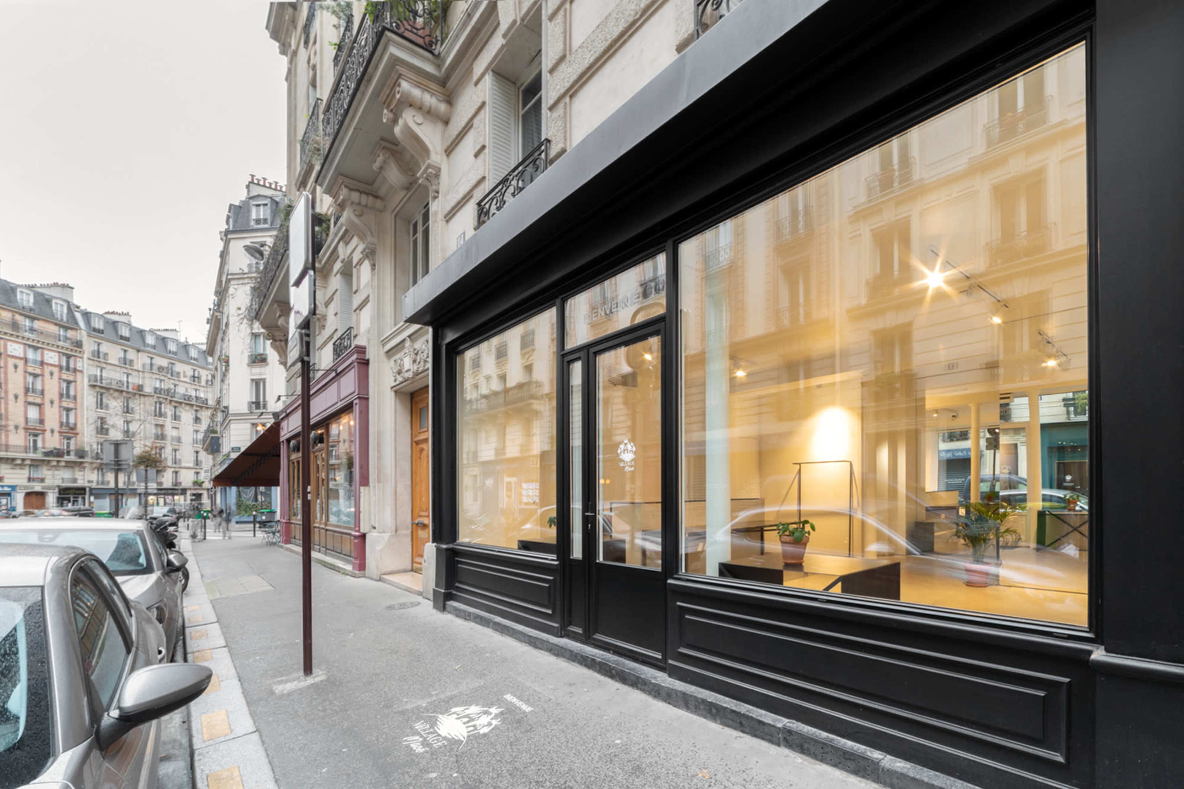 A storefront with large windows is located on a city street, alongside parked cars and nearby buildings.