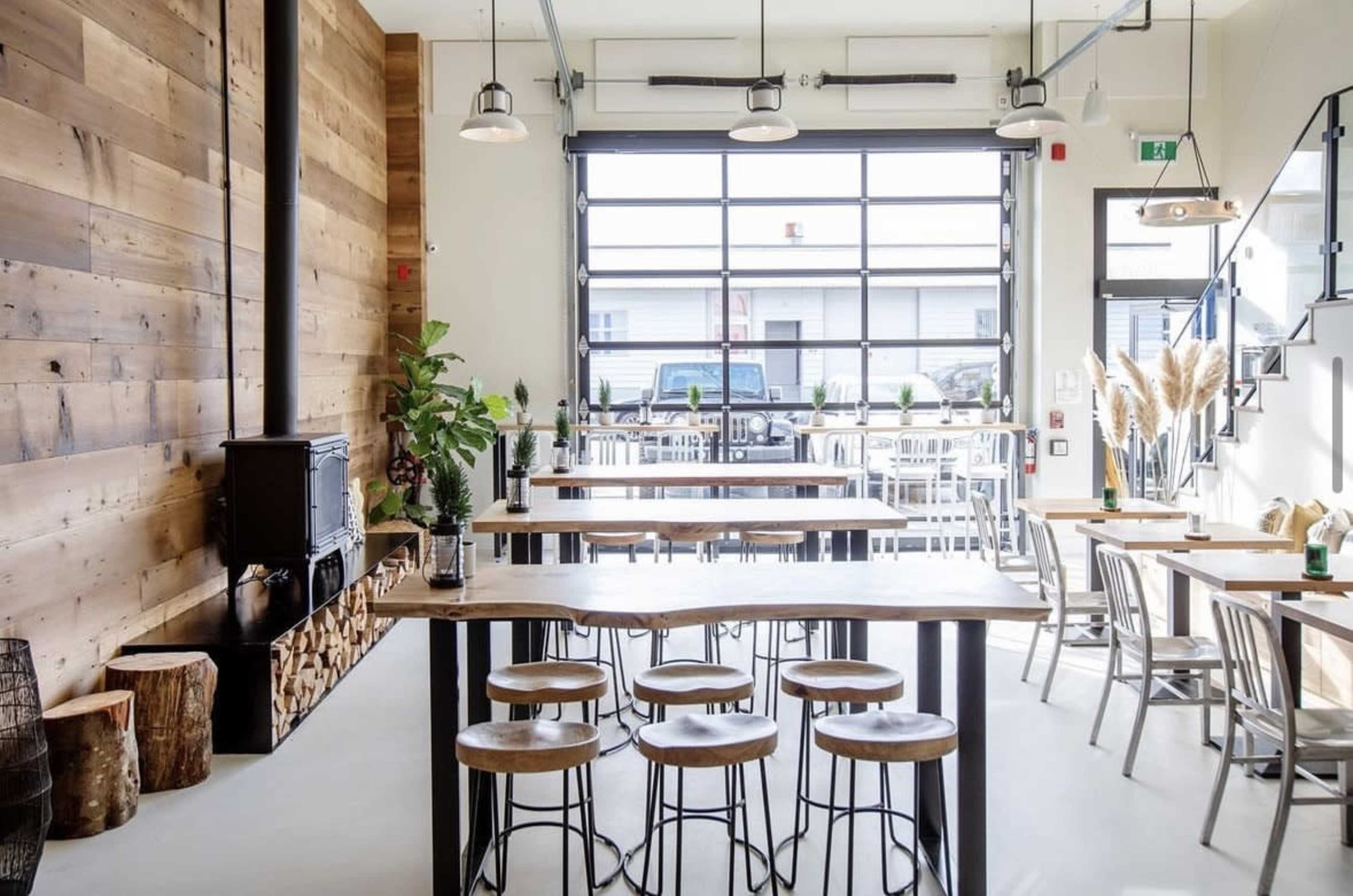 A modern café interior with wooden walls, long tables, and bar stools, featuring large windows that provide natural light.