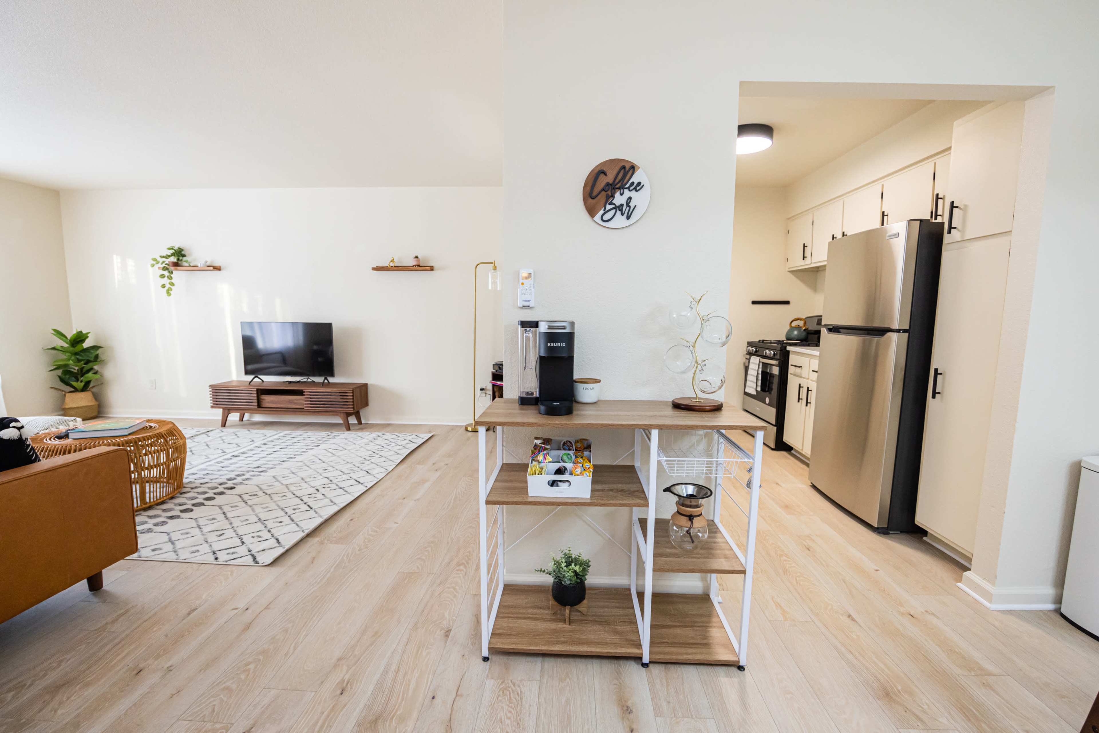 A modern, open-concept living area with a coffee station, a television, and a kitchen featuring stainless steel appliances.