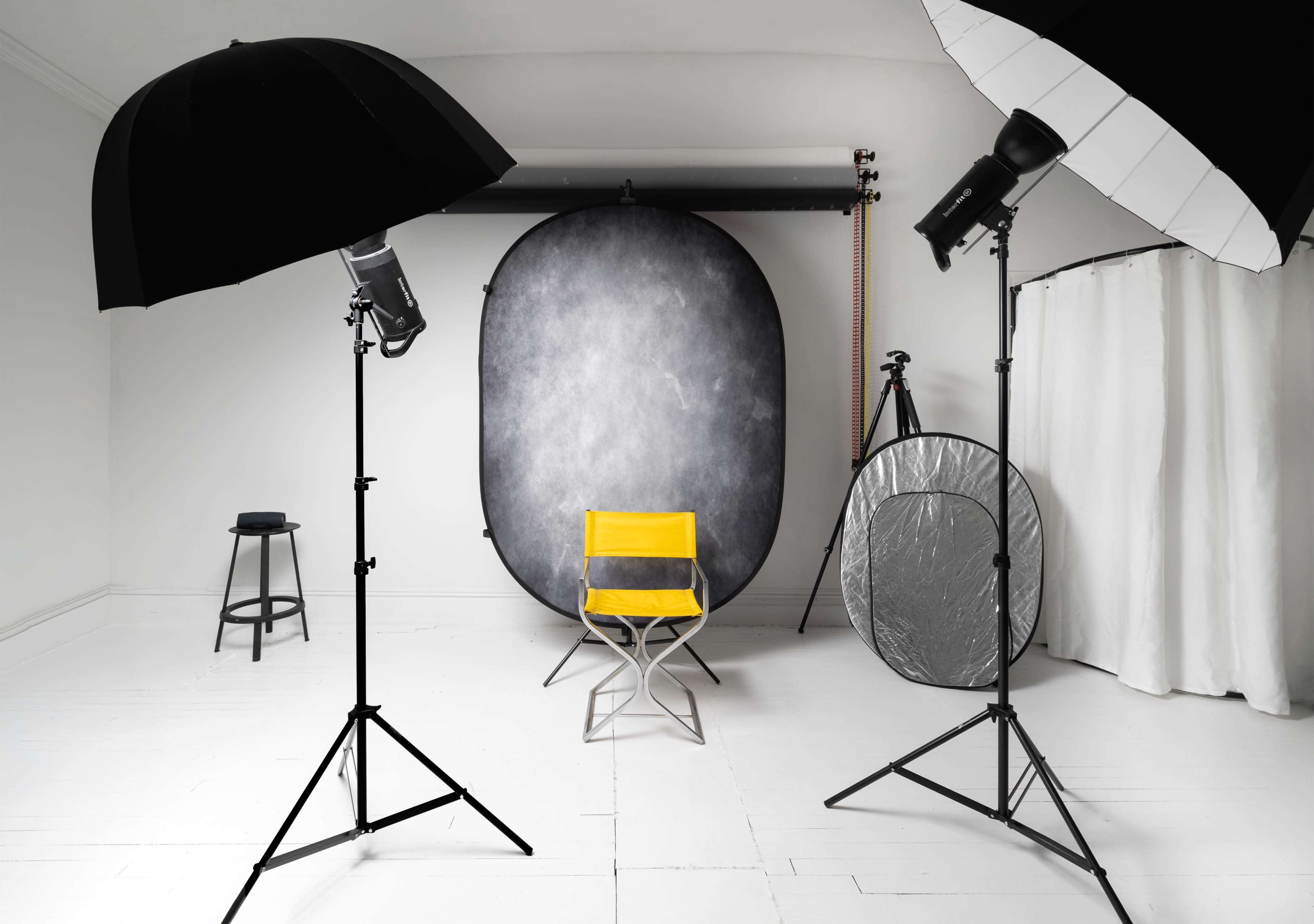 A photography studio is set up with lighting equipment, a backdrop, and a single yellow chair in the center.