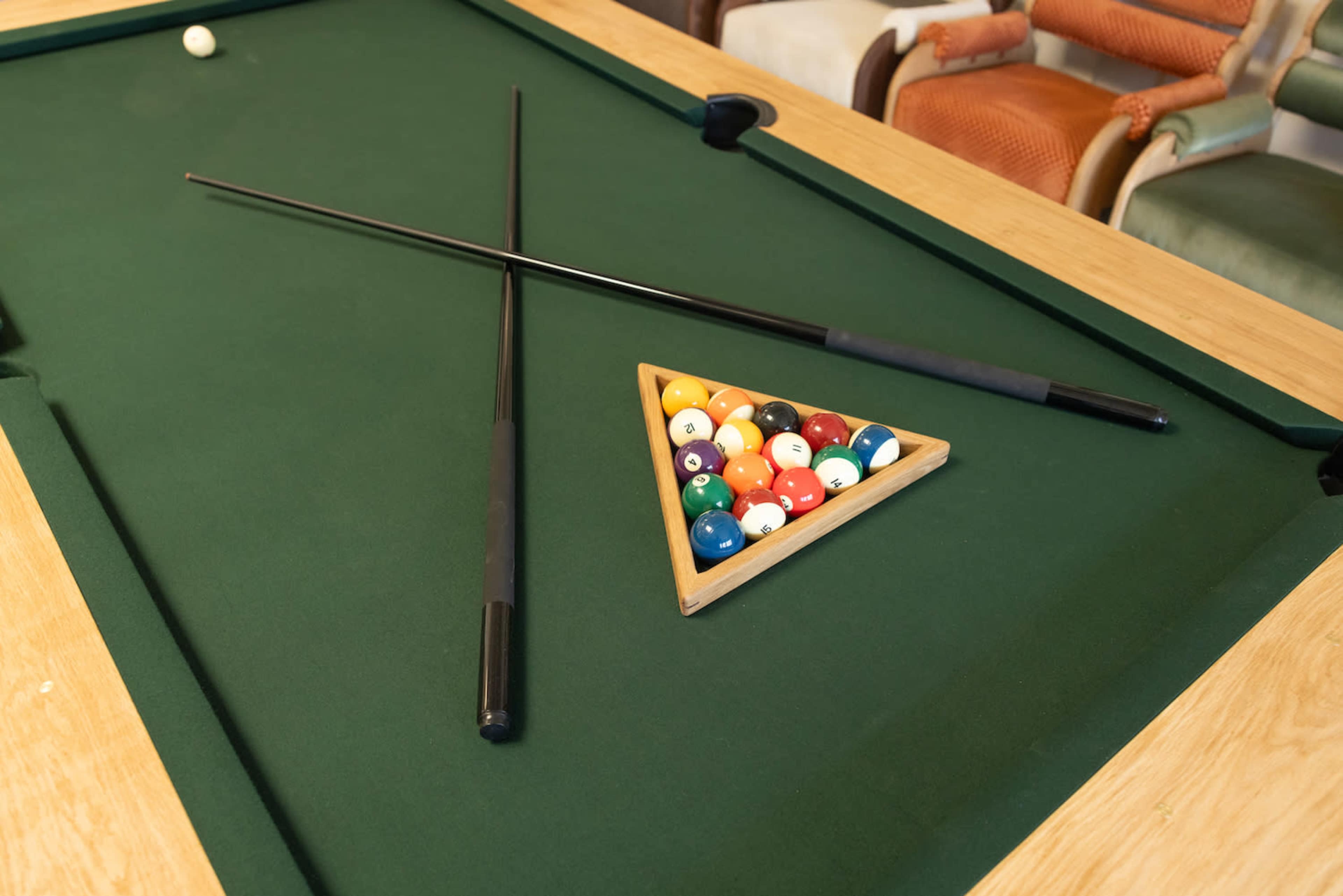 A green felt pool table with two cue sticks crossed over a triangle of colored billiard balls.