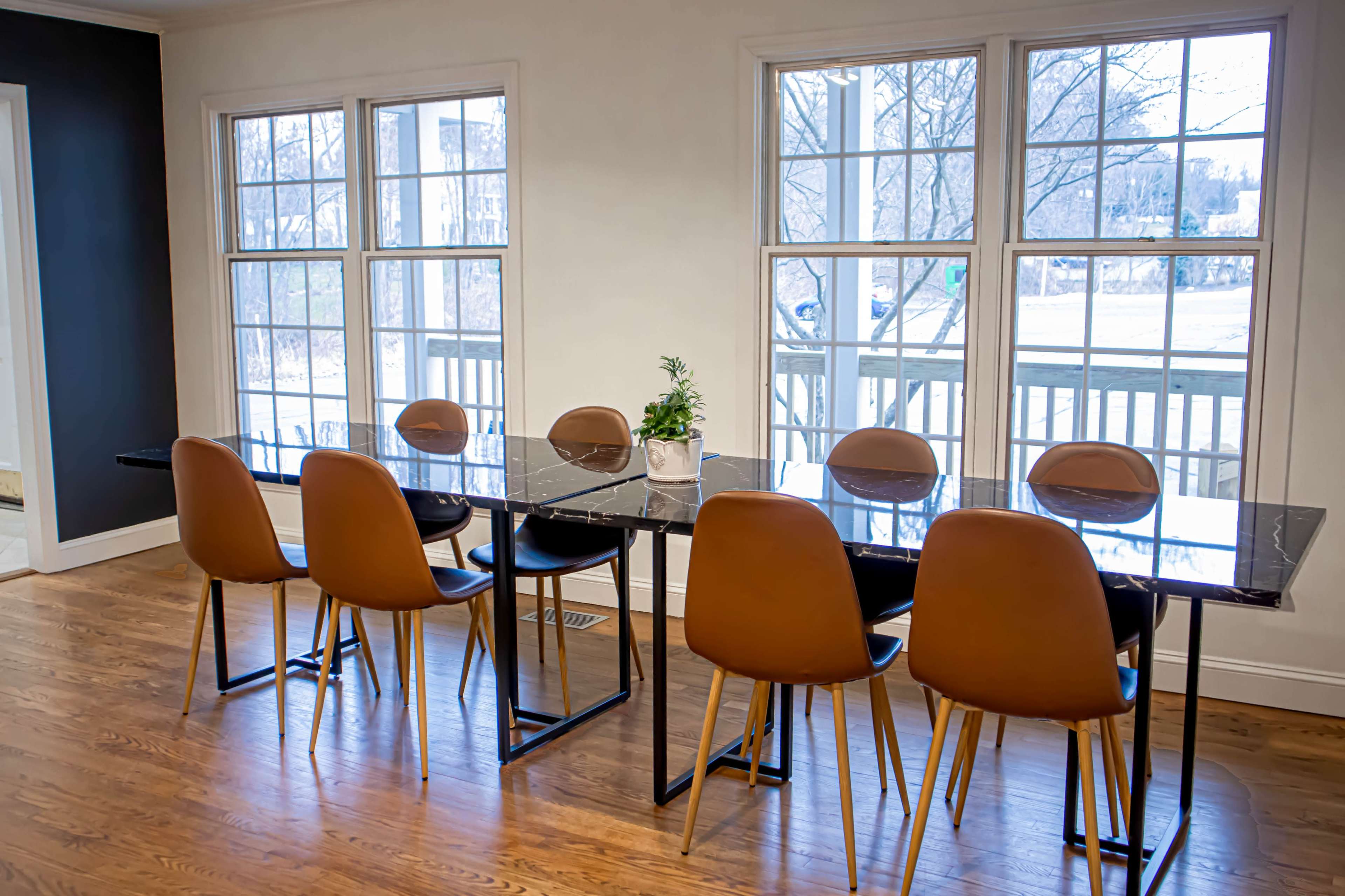 A long, dark table with eight brown chairs is set near large windows, allowing natural light to fill the room.