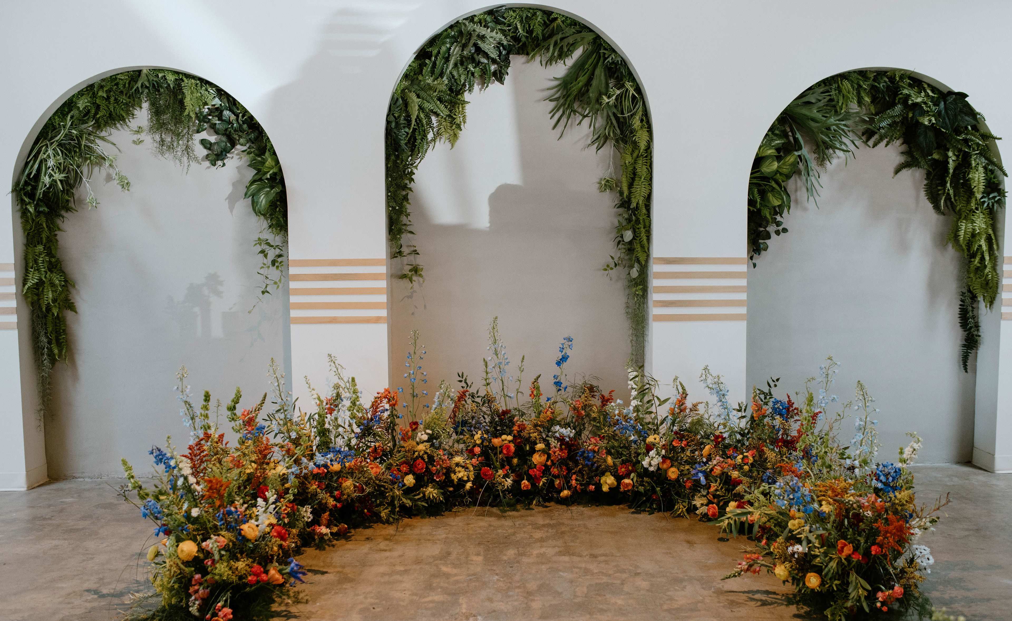 The image shows a decorative area featuring three archways adorned with greenery and flowers arranged in a semicircular display on the floor.