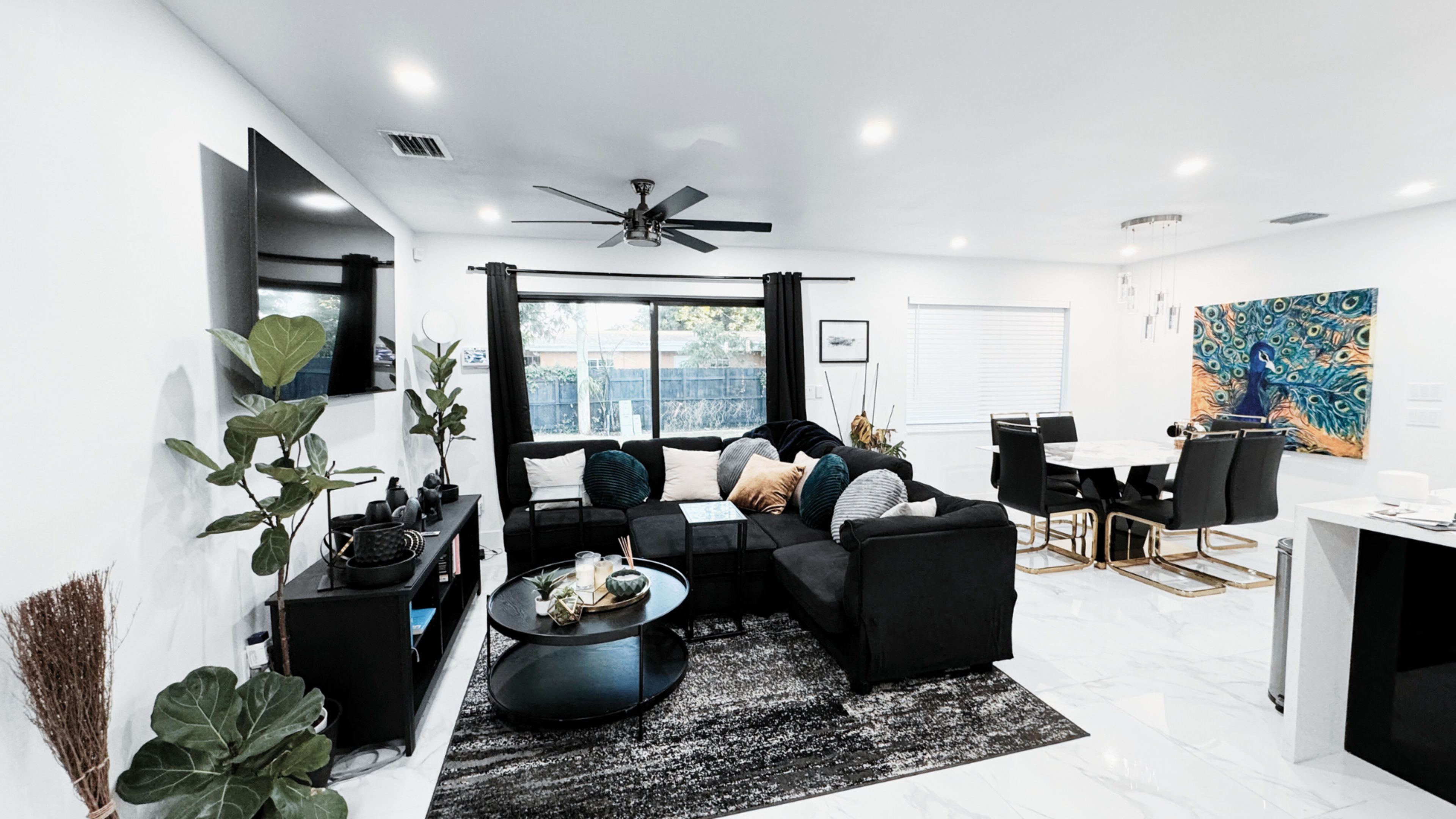 The living room features a black sectional sofa, a round coffee table, and a dining area with a large painting on the wall.