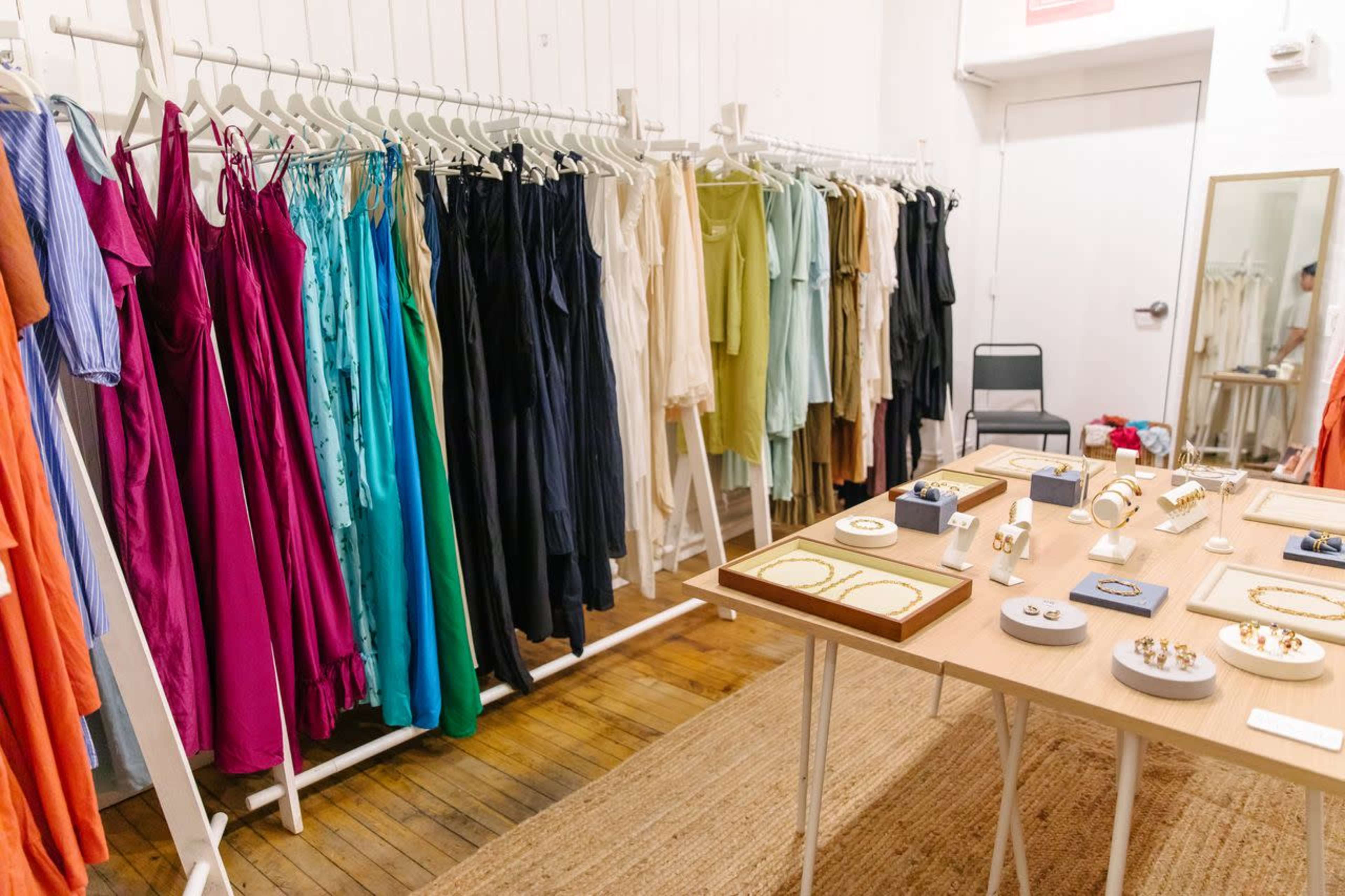 The image shows a clothing boutique with a rack displaying a variety of dresses in different colors and a table featuring an assortment of jewelry items.