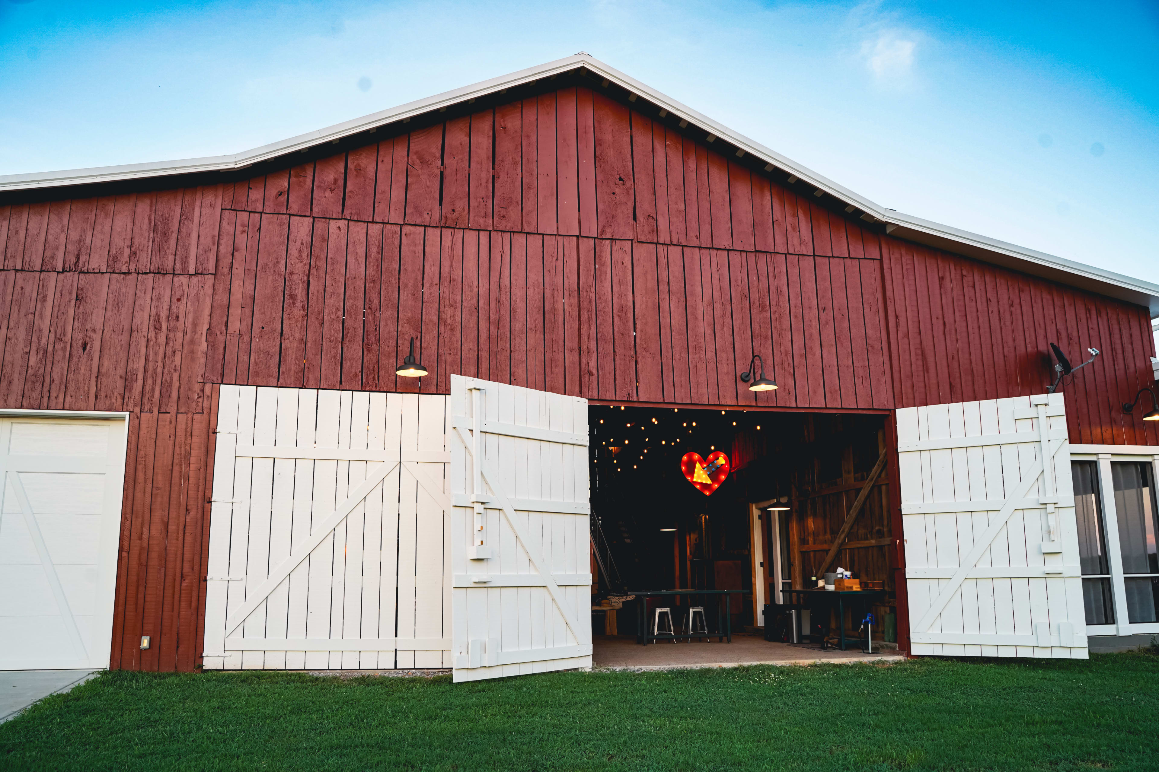 A red barn with white double doors is open, revealing a heart-shaped light fixture hanging inside.
