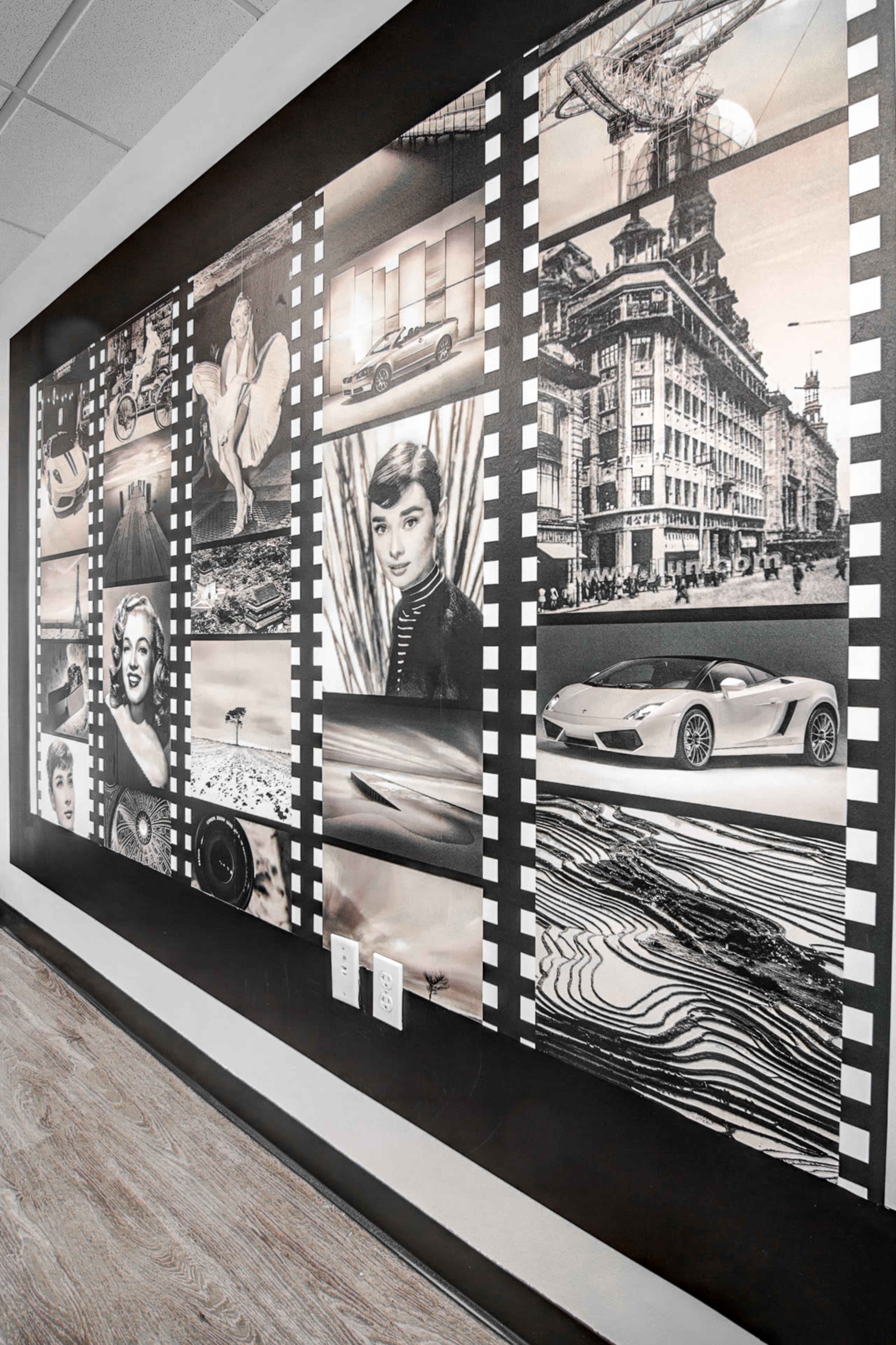 A black and white mural composed of various filmstrip-like sections showcasing classic Hollywood icons, vintage cars, and architectural scenes.