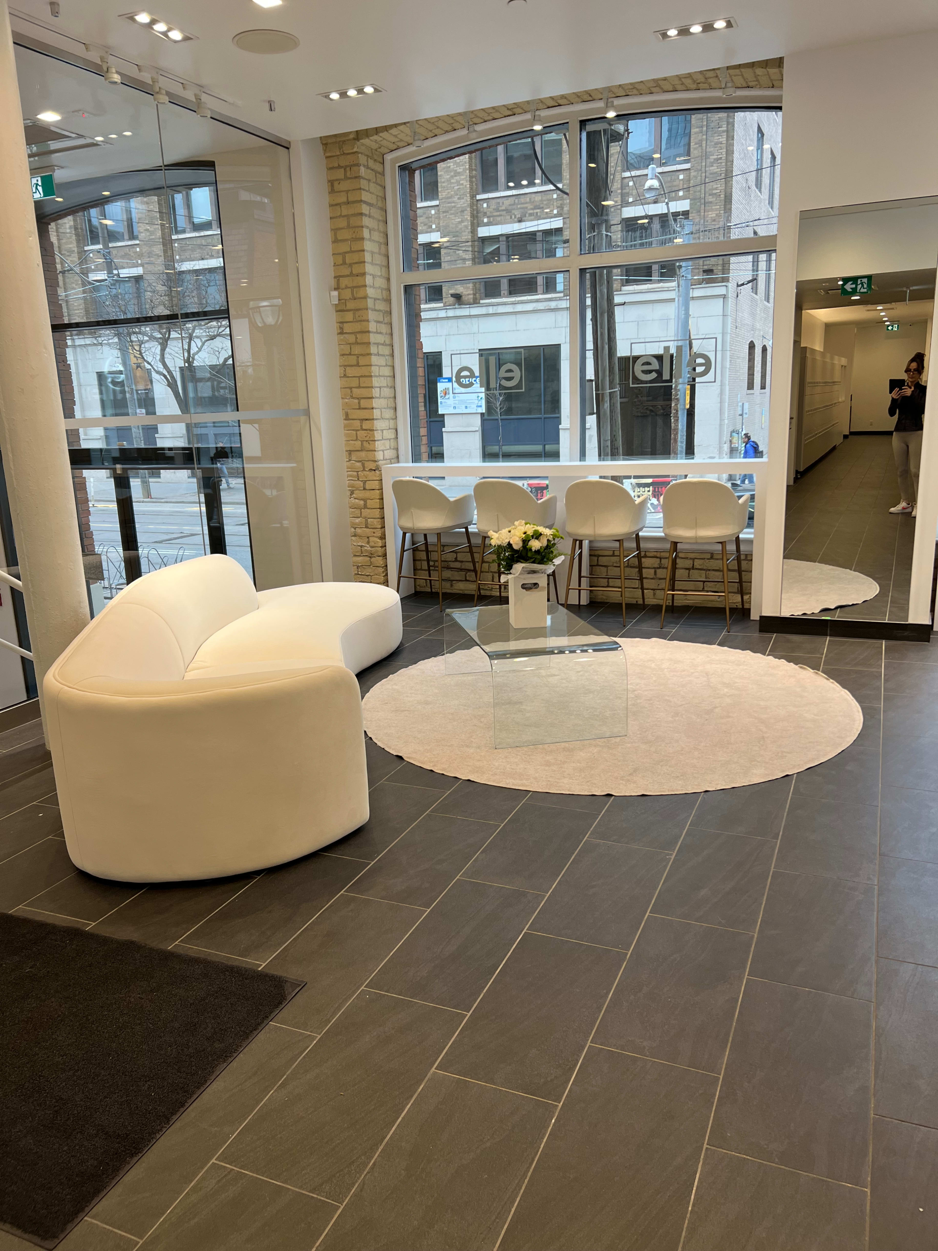 A modern lobby area with a white curved sofa, a round rug, a glass coffee table, and a seating arrangement featuring white chairs.