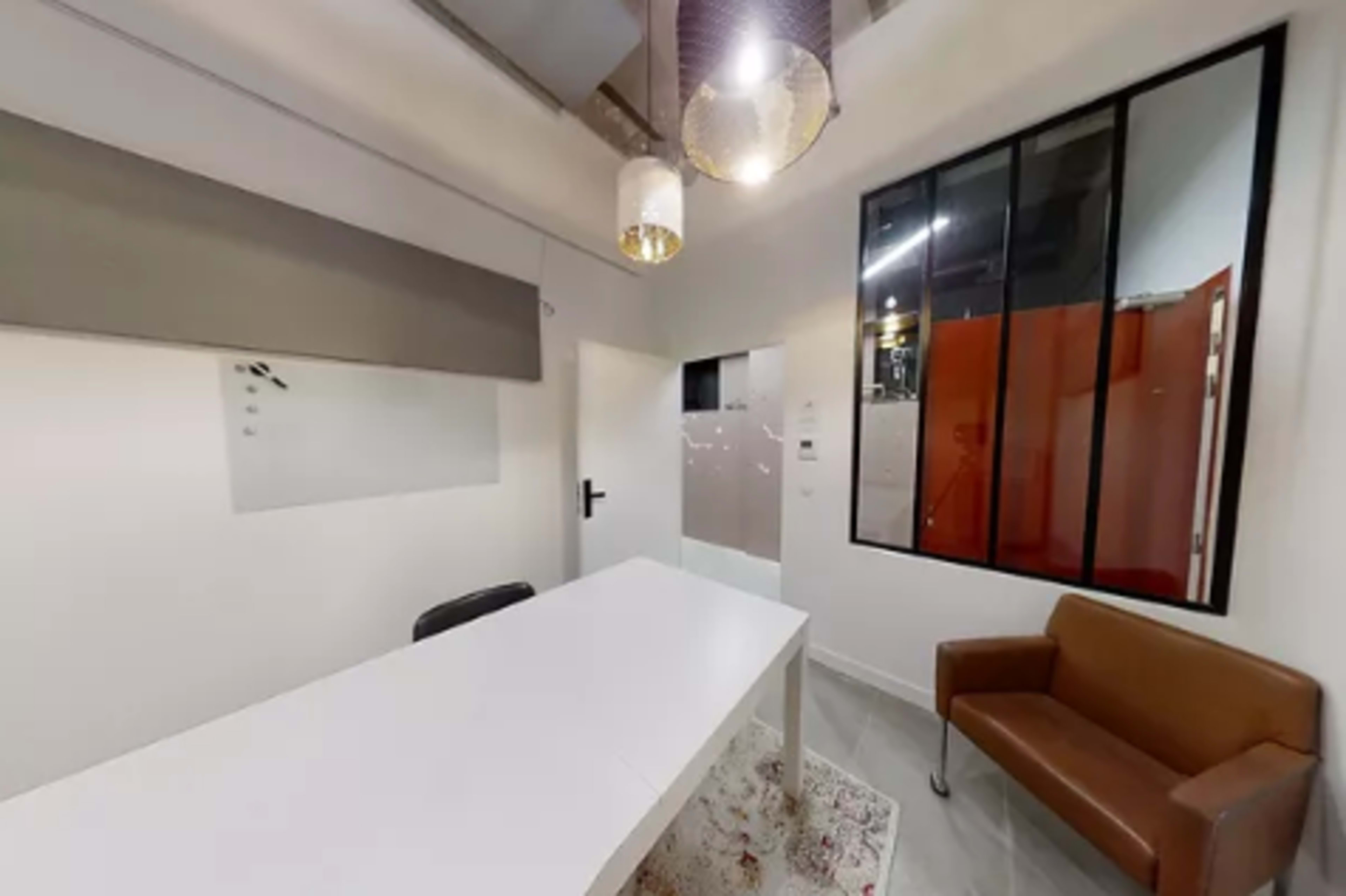 A modern office space featuring a white table, a brown leather chair, and large windows with black frames.
