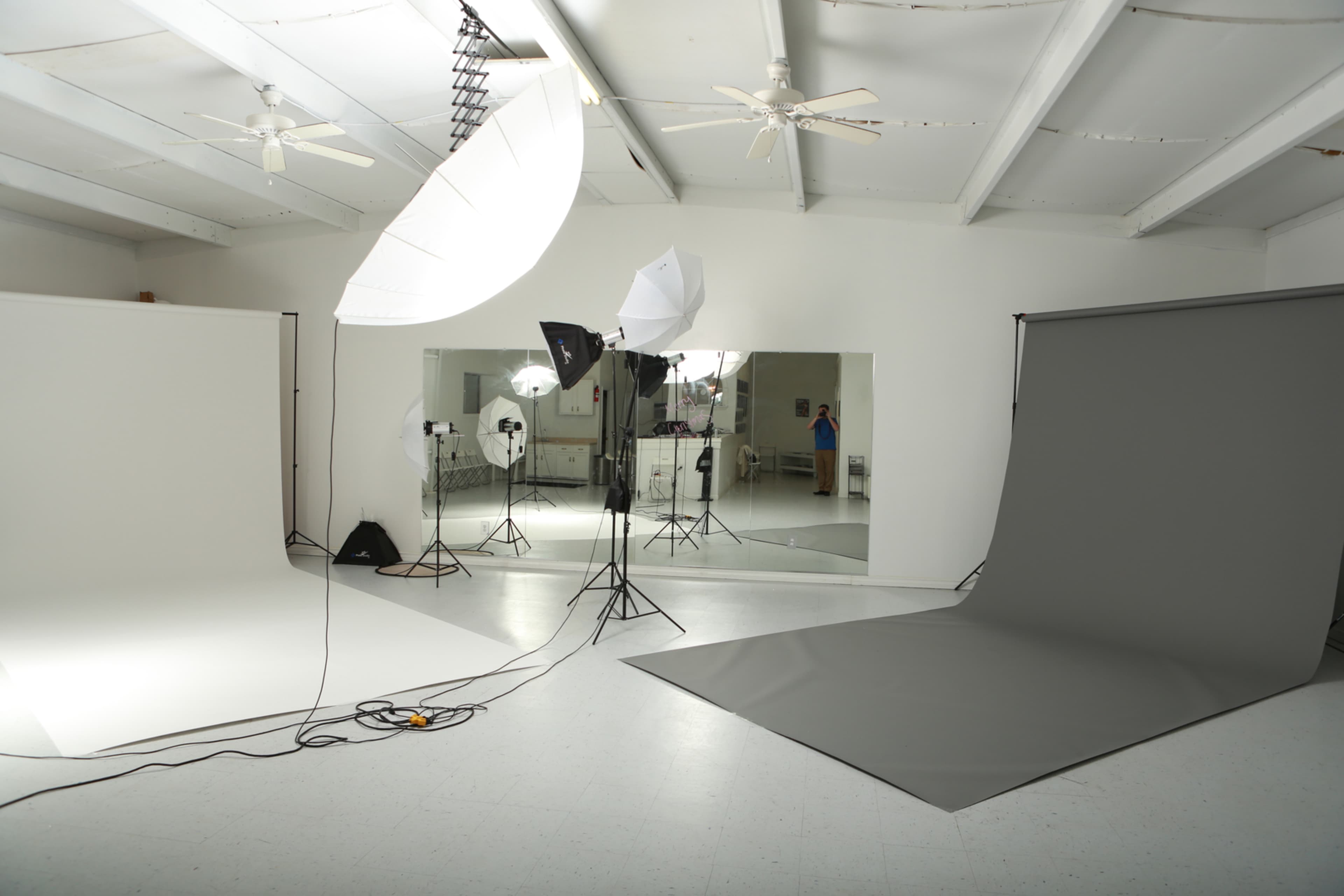 A photography studio features a white backdrop, a gray backdrop, and various lighting equipment set up around mirrors.