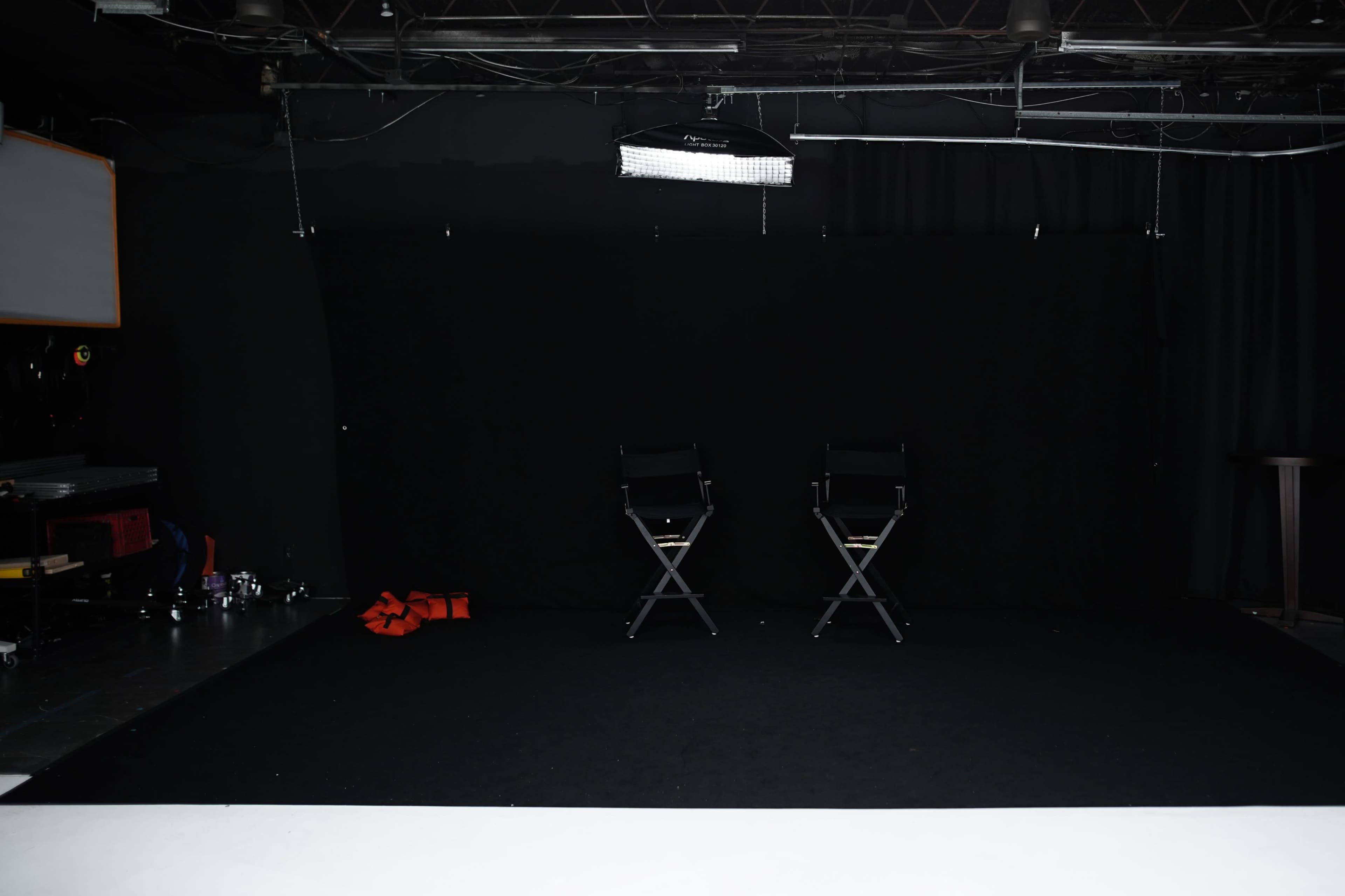 A dimly lit studio space with two black director's chairs facing each other on a black floor.