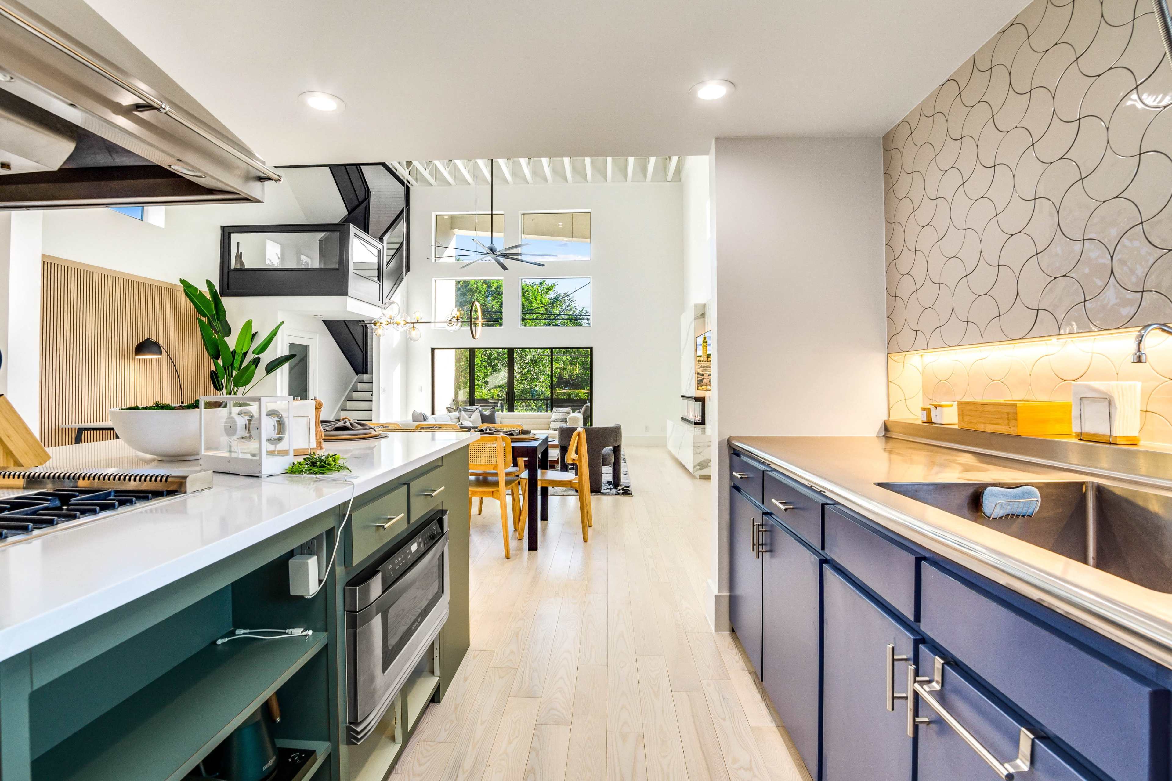 A modern kitchen features a stainless steel stove, blue cabinetry, and a view of a dining area with large windows.