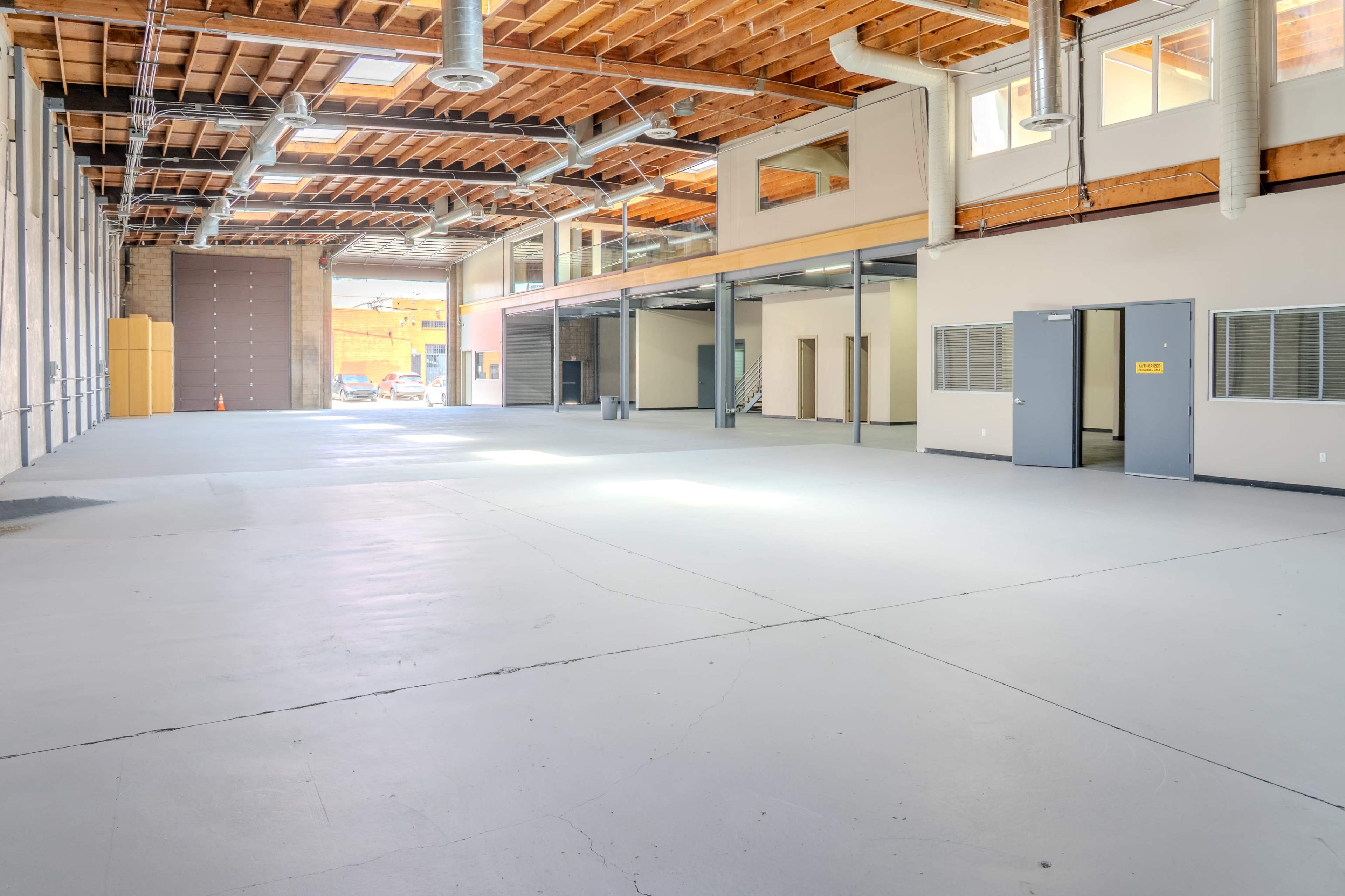 The image shows a spacious, empty warehouse with high ceilings, polished concrete flooring, and large windows allowing natural light to enter.