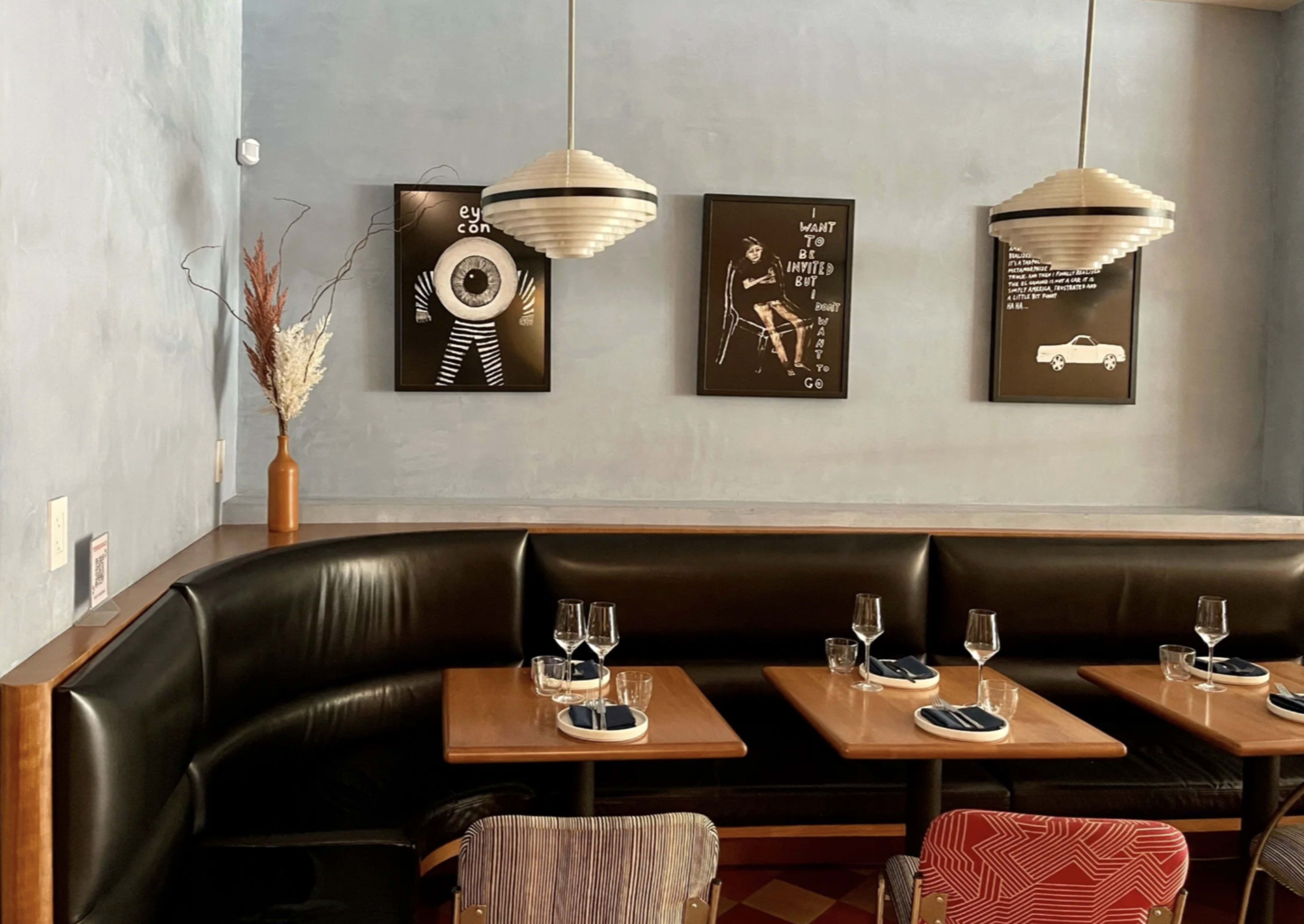The image shows a cozy restaurant corner with dark leather seating, wooden tables, and framed artwork on the walls.