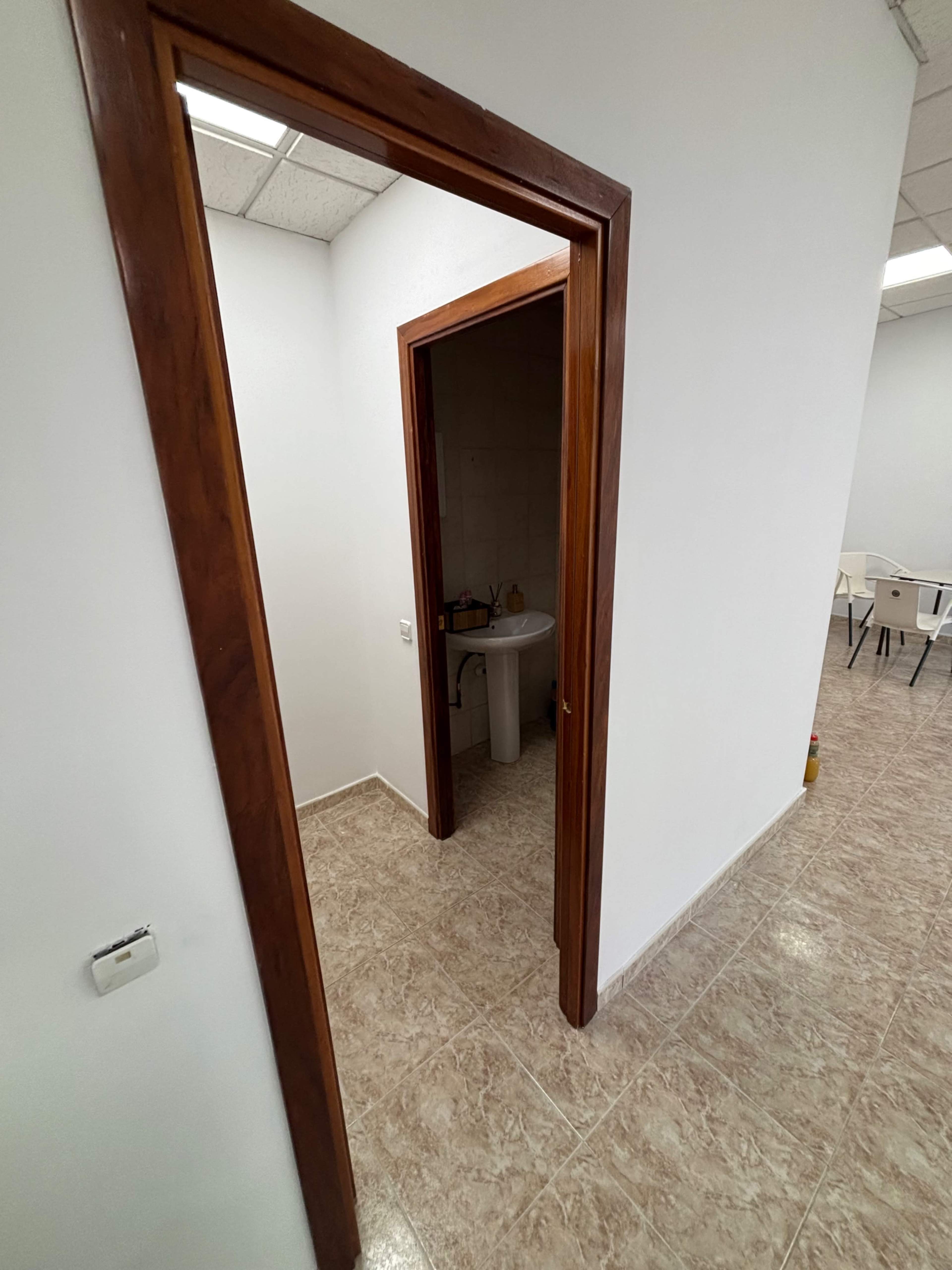 The image shows a hallway with a wooden door frame leading to a small bathroom area and another room in the background.