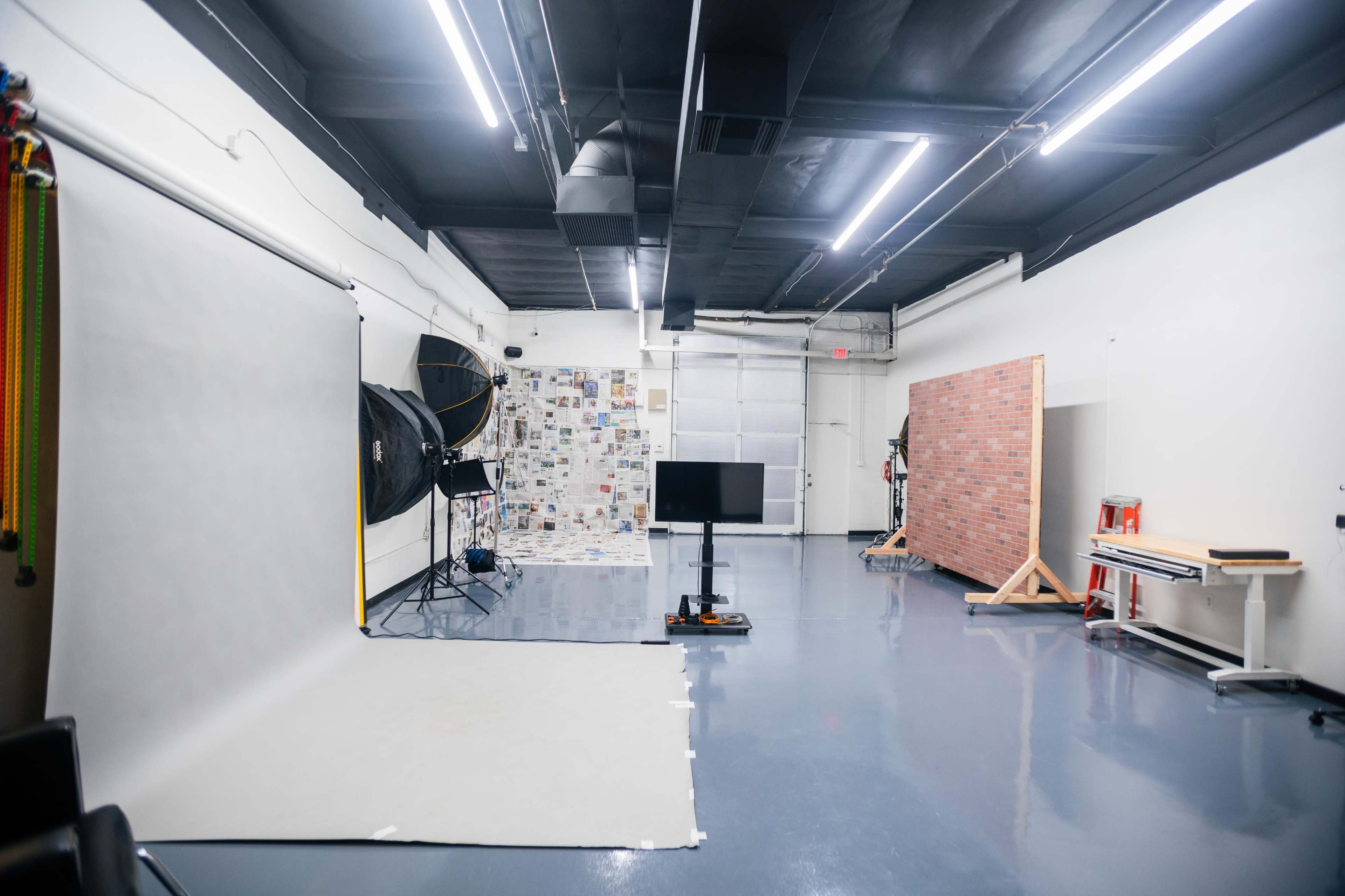 A photography studio with a seamless backdrop, a large softbox, a television monitor on a stand, and various props against a white wall.