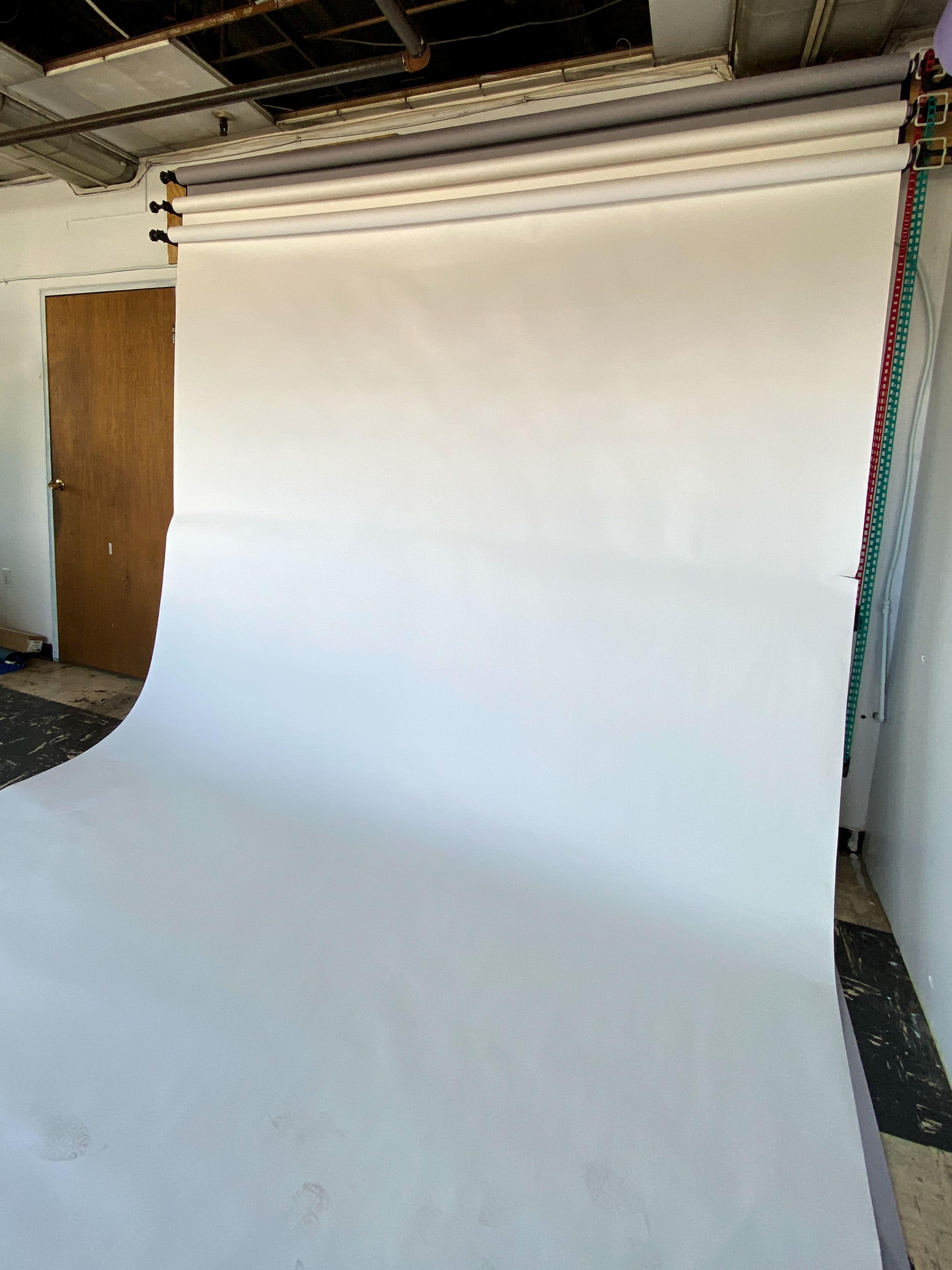 A photography studio with a large white backdrop rolled out against a plain wall and a wooden door in the background.