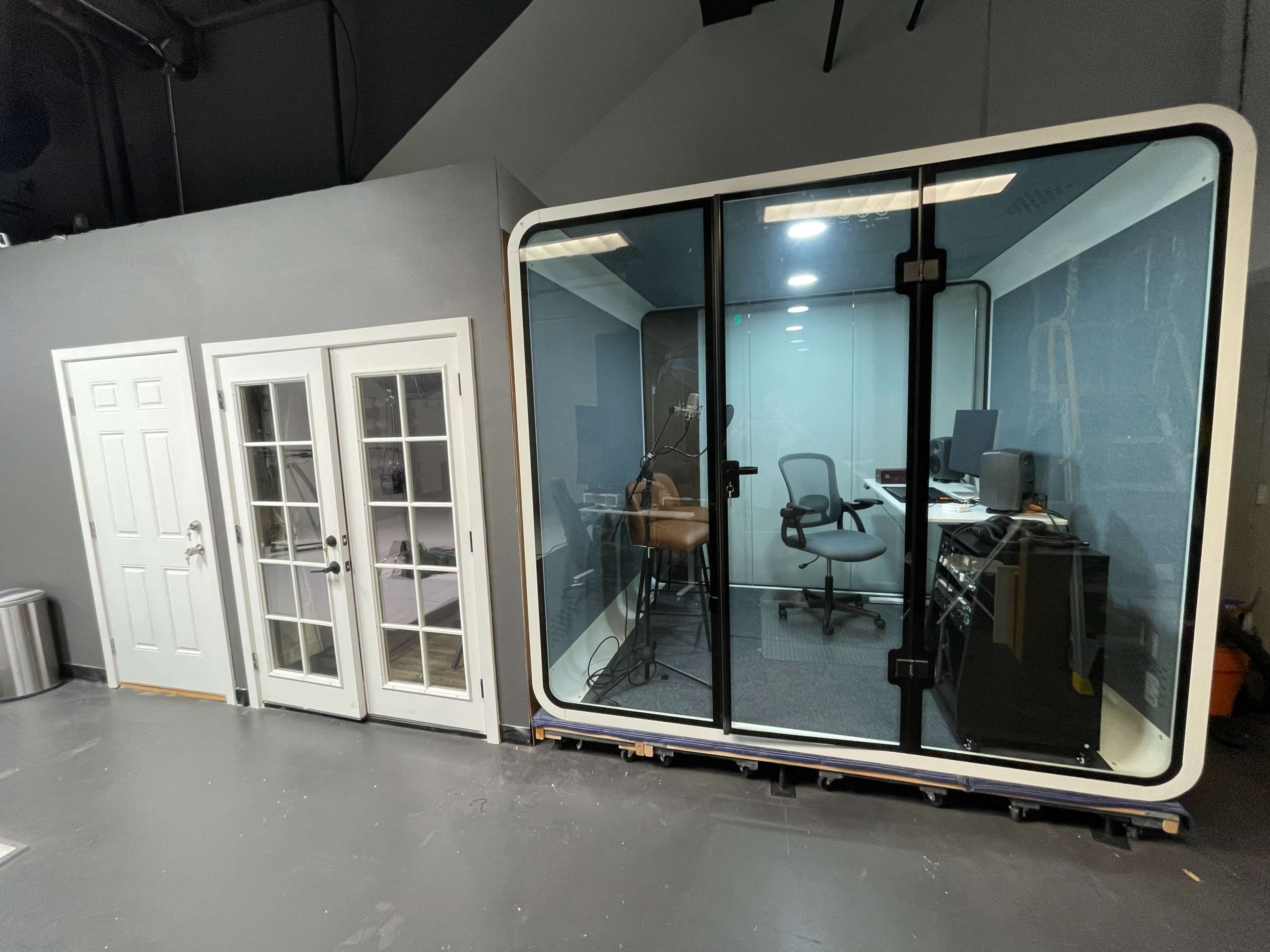 The image shows a modern recording booth with glass walls beside a set of double doors in a room.