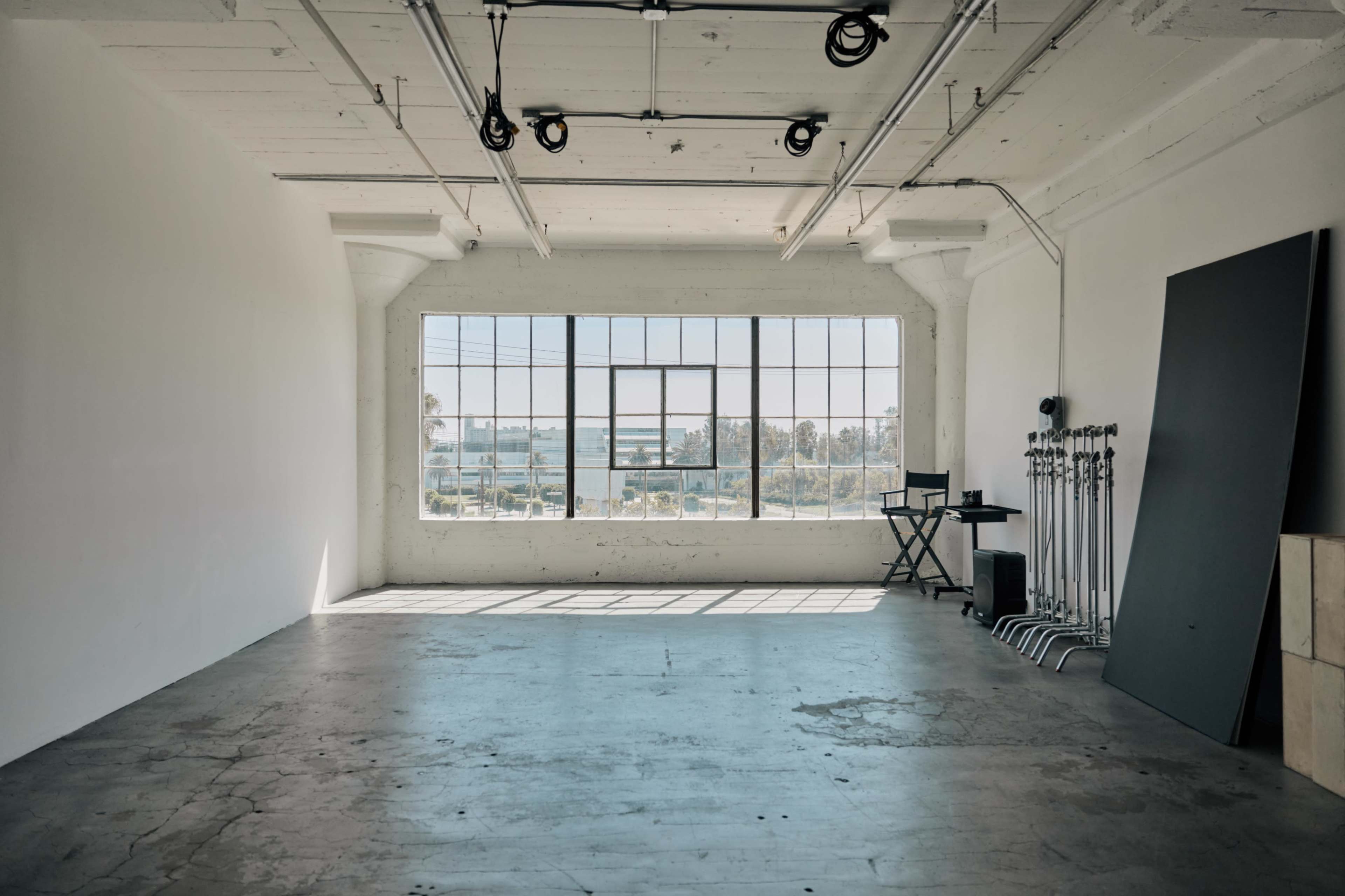 An empty studio space features a large window with a view, concrete flooring, and minimal furnishings.