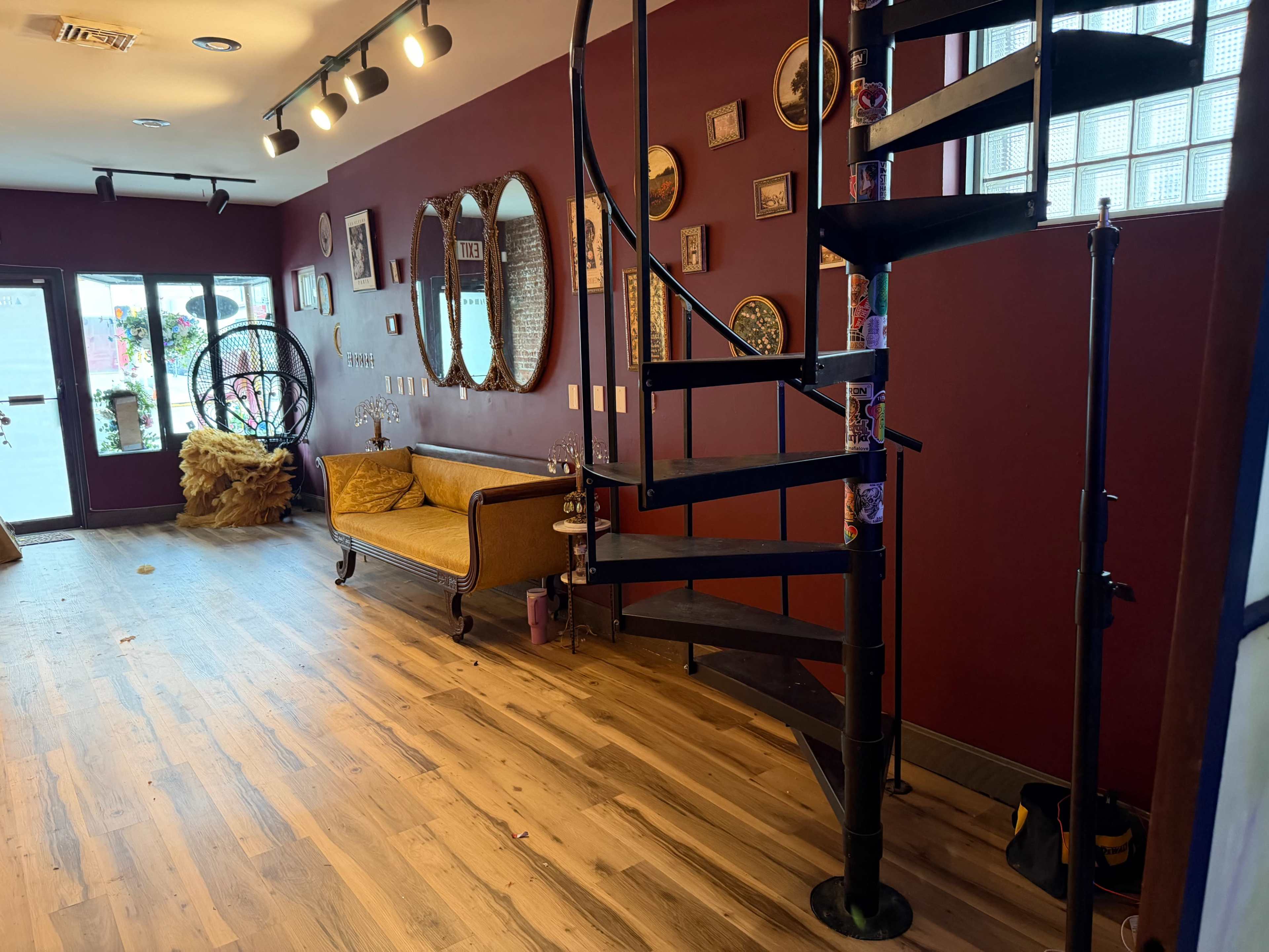 The image shows a cozy room with a spiral staircase, a vintage-style couch, and various decorative wall elements, all complemented by wooden flooring.