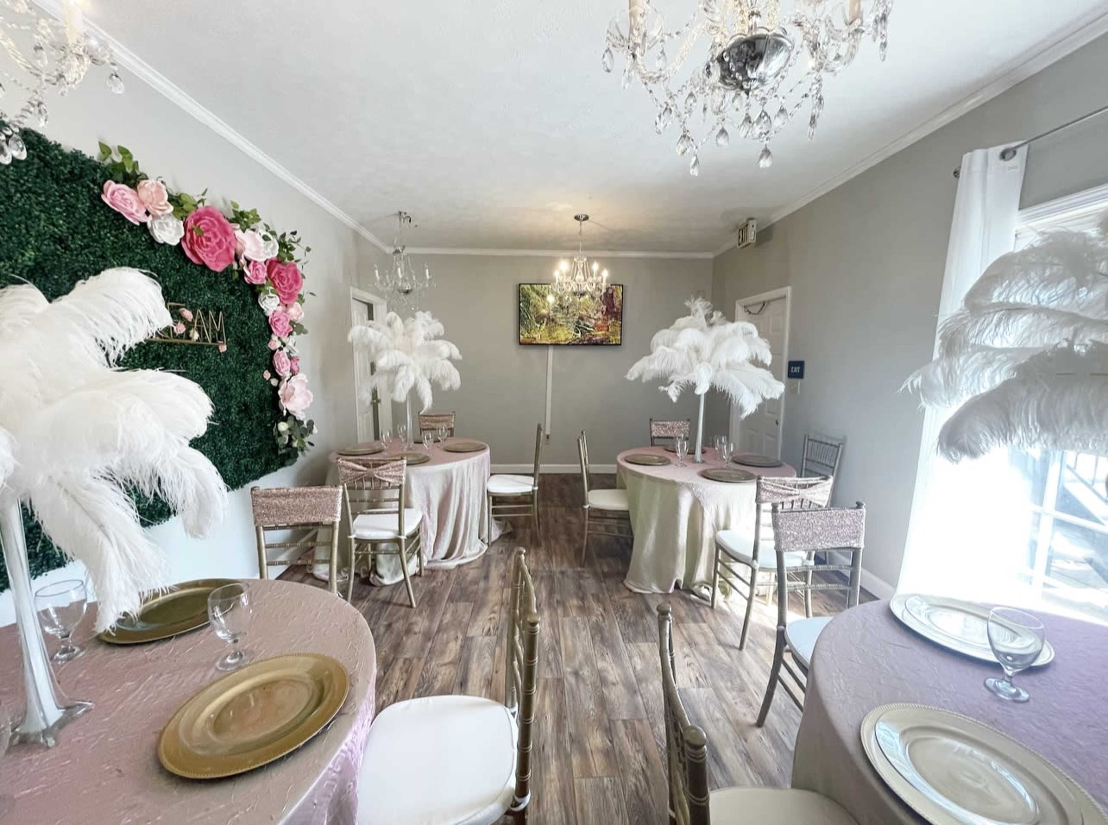 A stylishly decorated dining room with round tables covered in pastel tablecloths, adorned with feather centerpieces and floral wall accents.