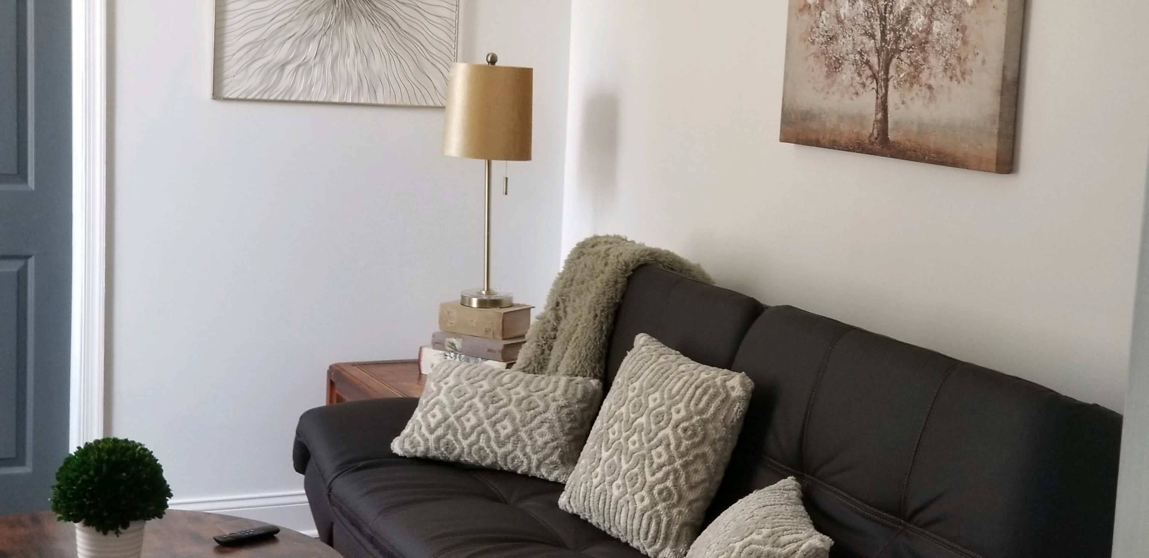 A living room with a black sofa, decorative pillows, a lamp, a plant, and artwork on the walls.