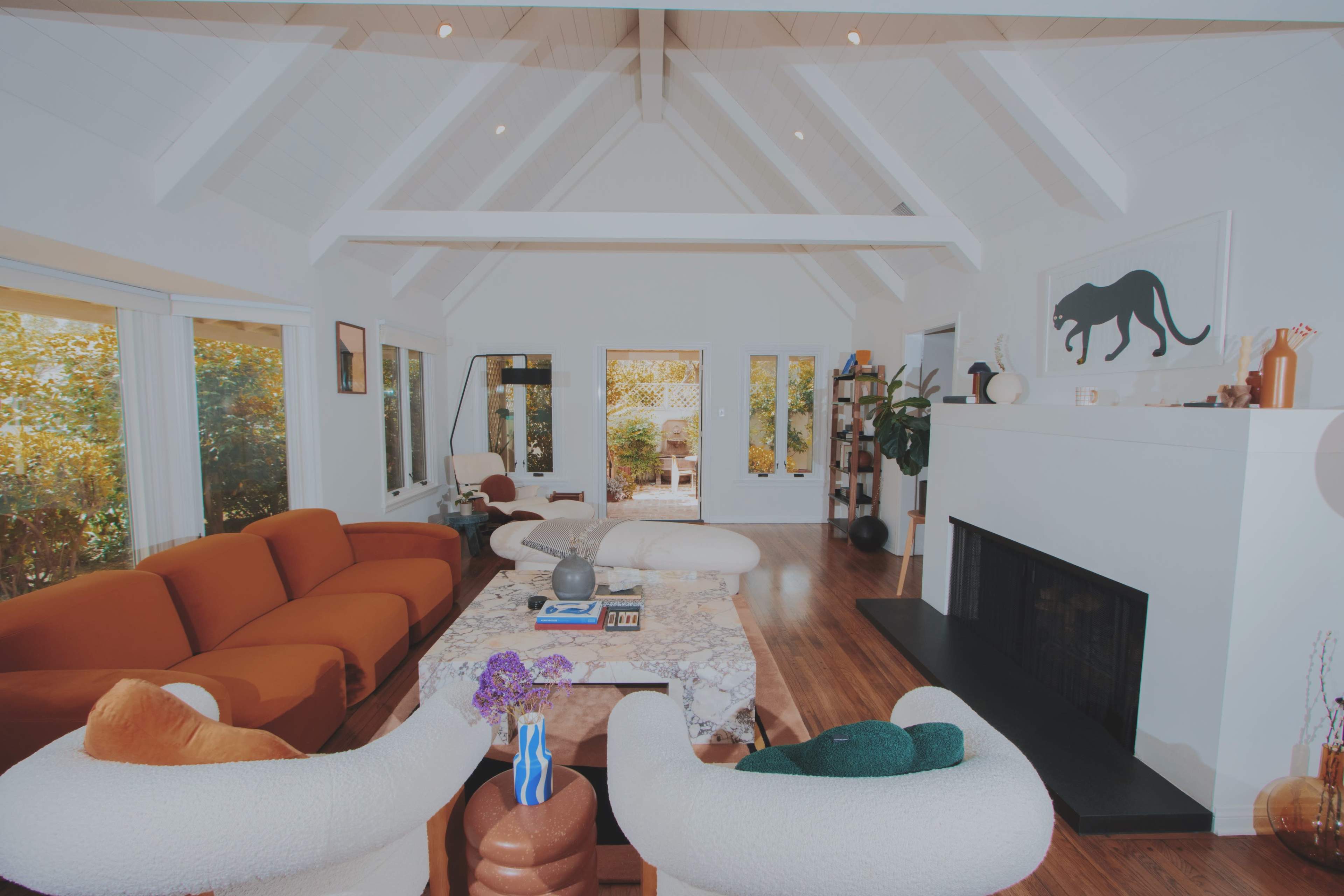 A spacious living room features a combination of modern furniture, a coffee table at the center, and large windows overlooking a garden.