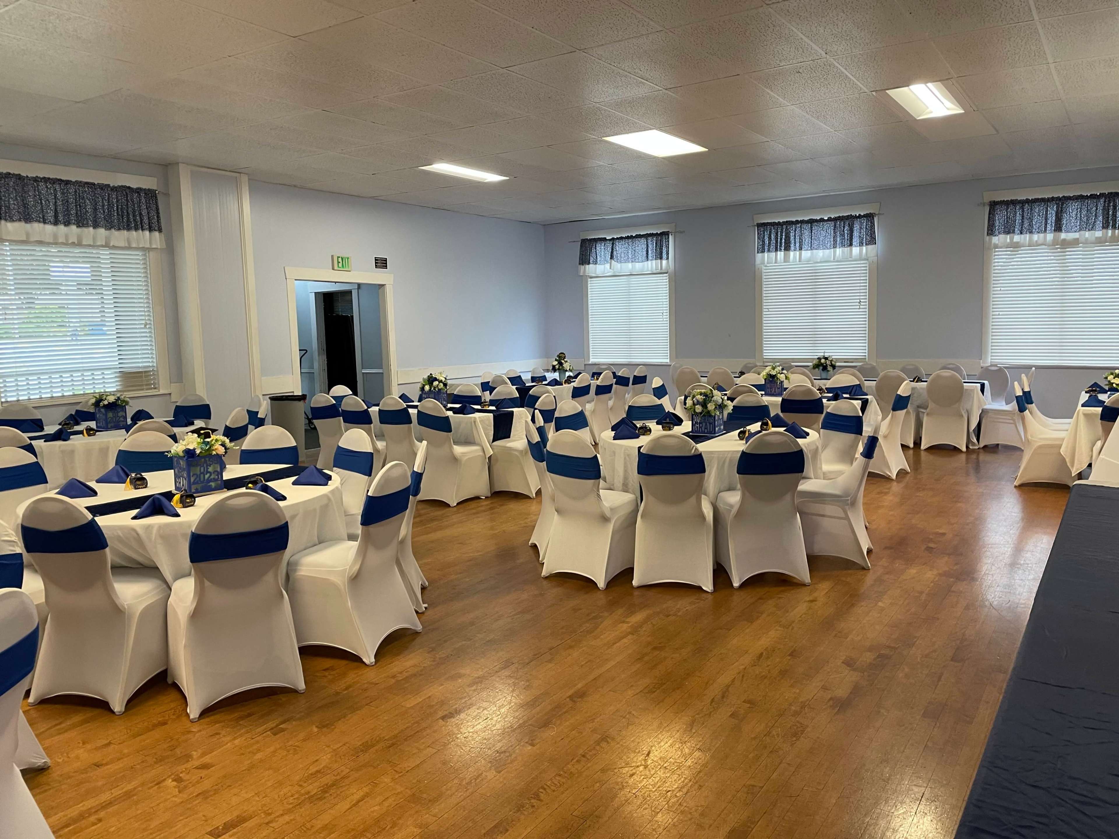 A banquet hall set up with round tables covered in white linens and blue chair sashes, arranged for an event.