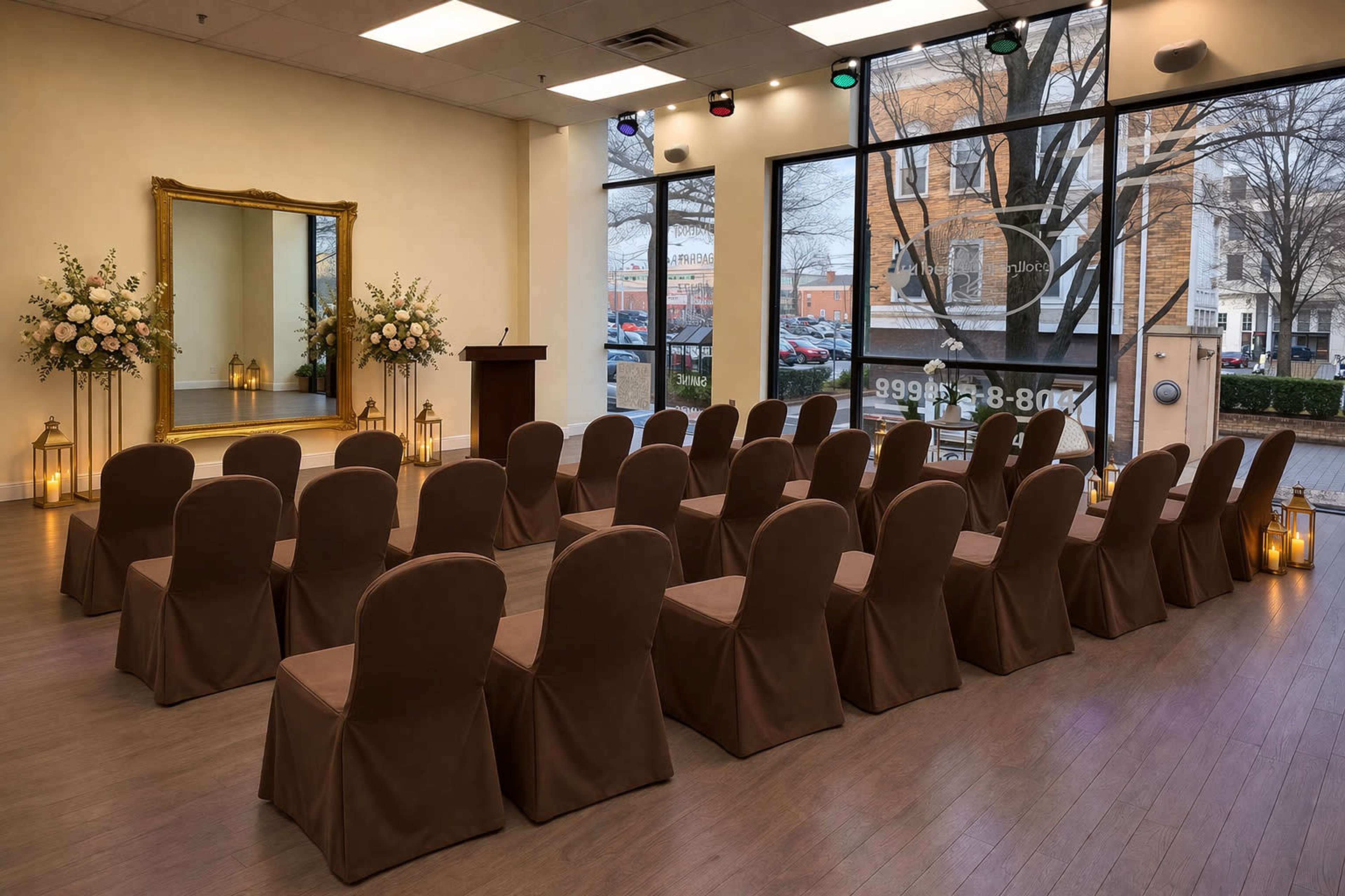 The image shows a spacious event room with rows of covered chairs facing a podium, surrounded by floral arrangements and decorative lanterns.