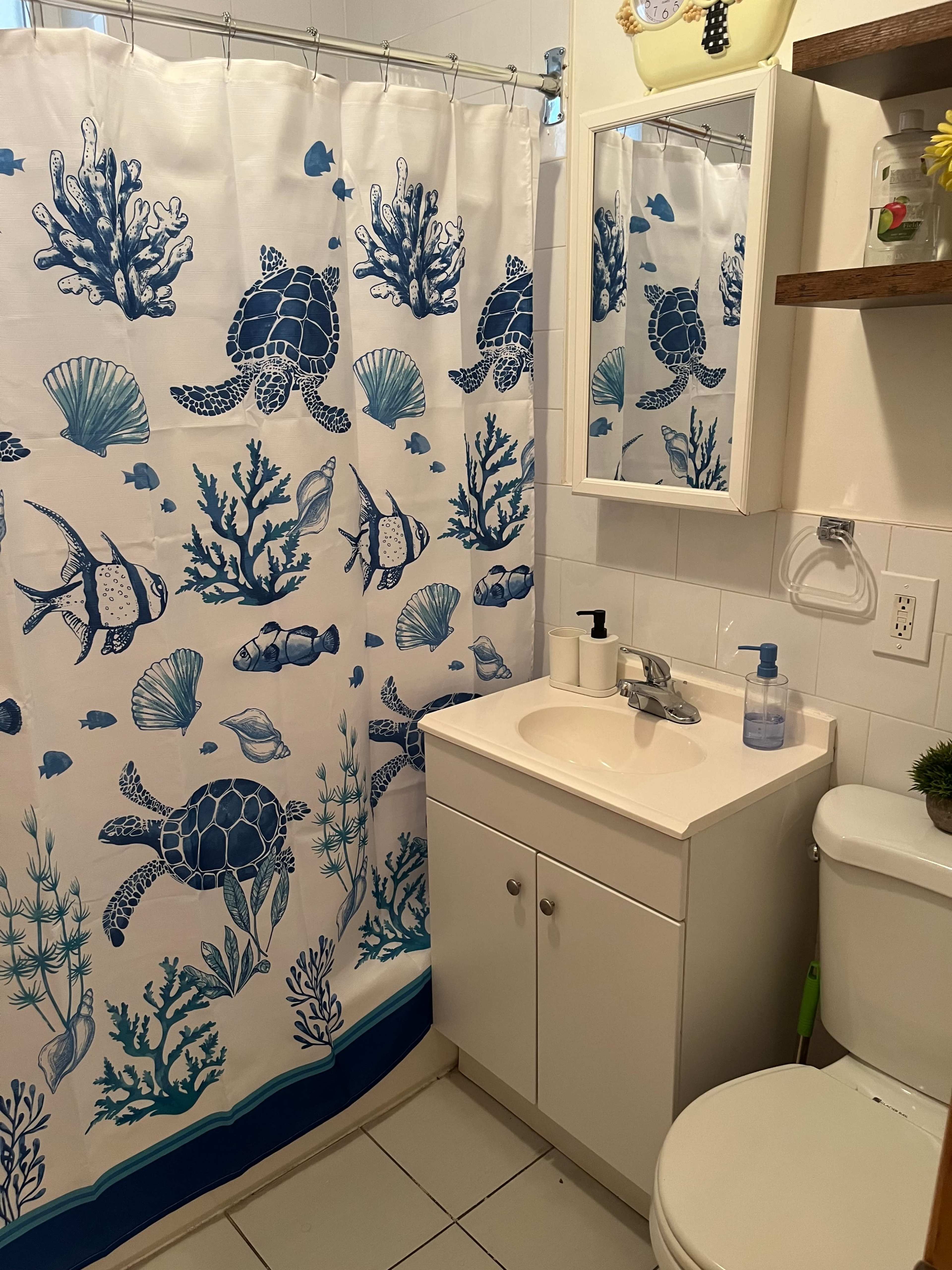 A bathroom featuring a shower curtain with ocean-themed designs, a white vanity with a sink, and a toilet nearby.