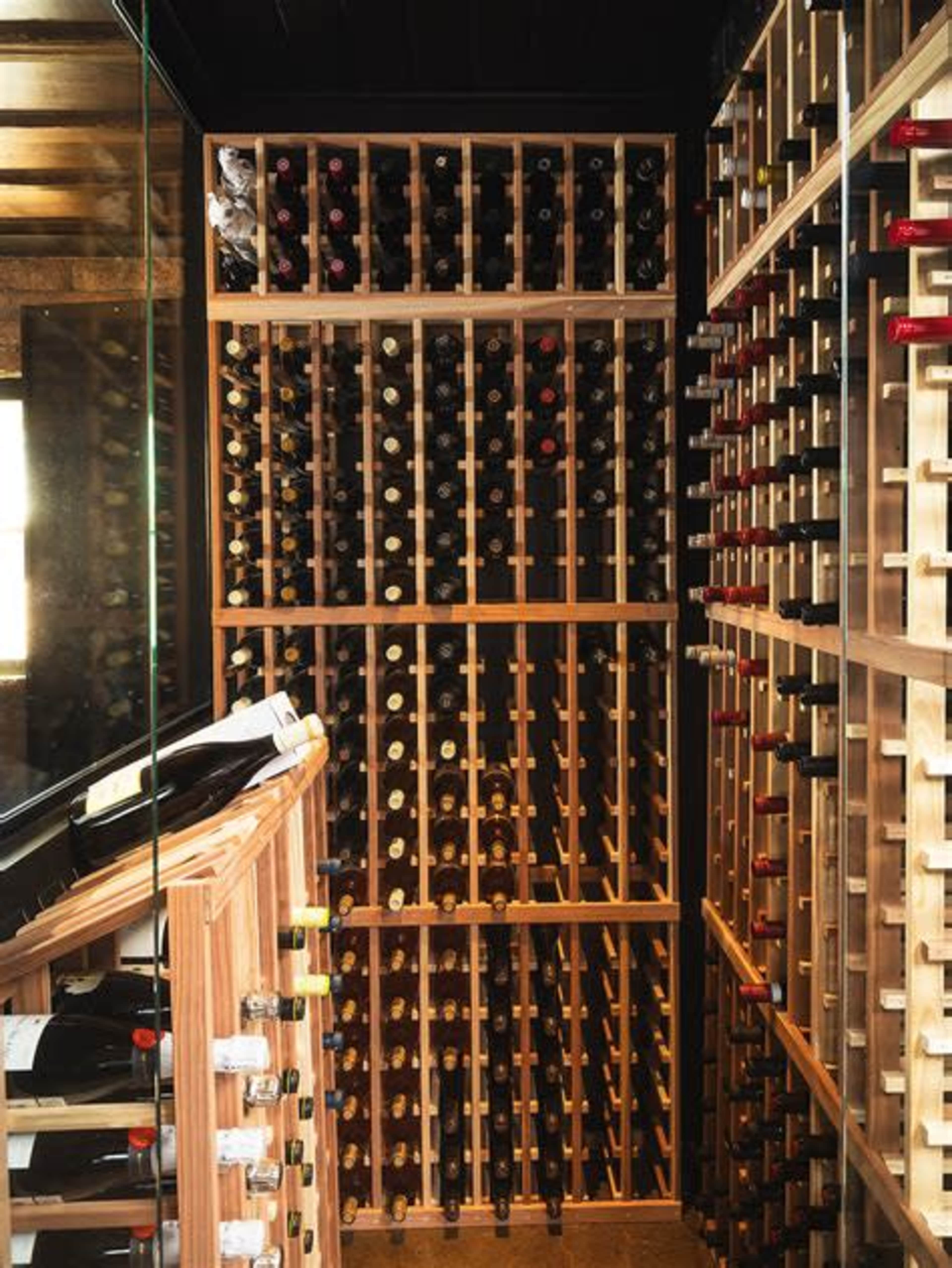 The image shows a wine cellar with wooden racks filled with various bottles of wine arranged neatly on the shelves.