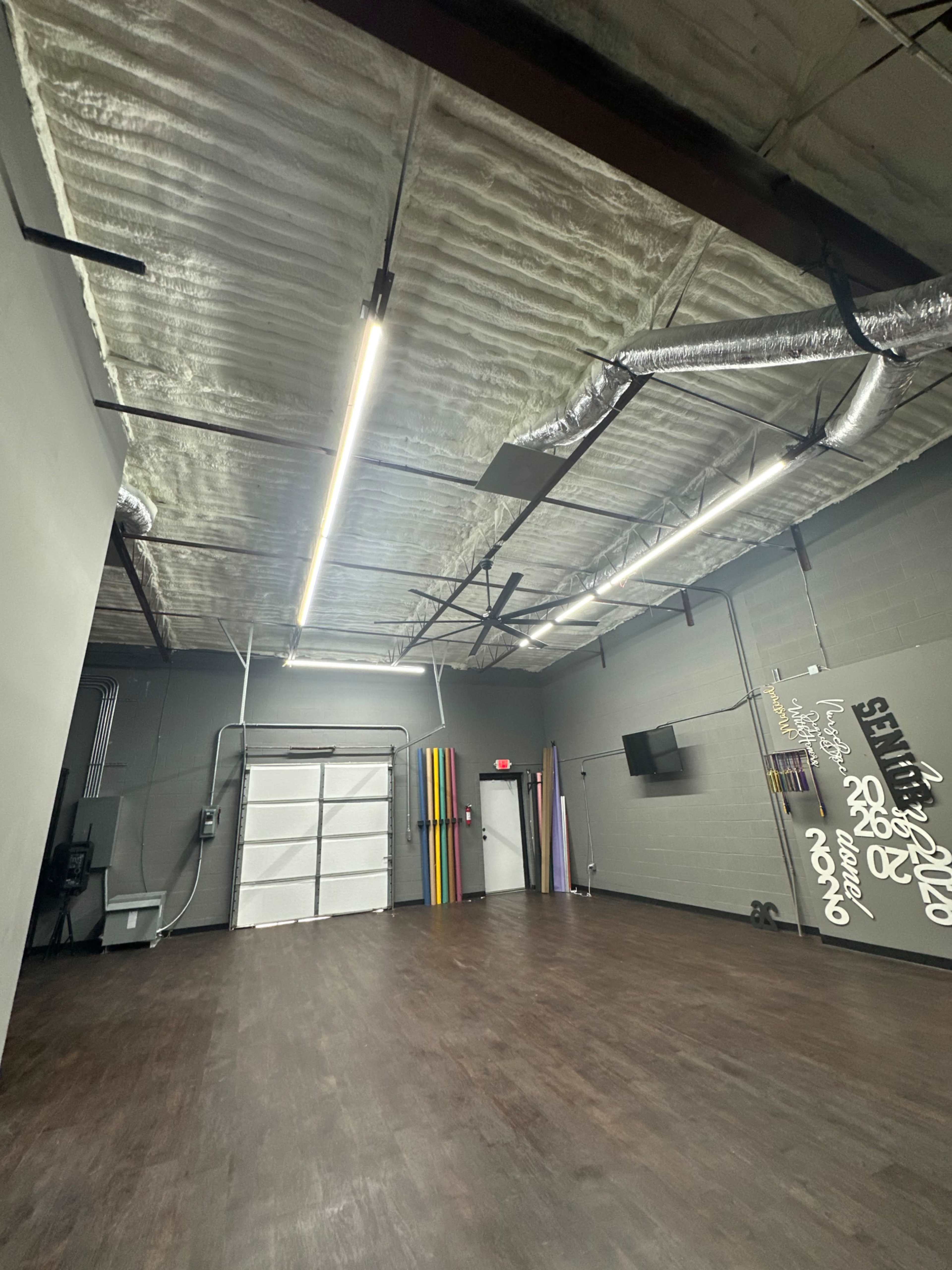 The image shows an empty industrial-style room with a high ceiling, fluorescent lighting, and colorful panels along one wall.