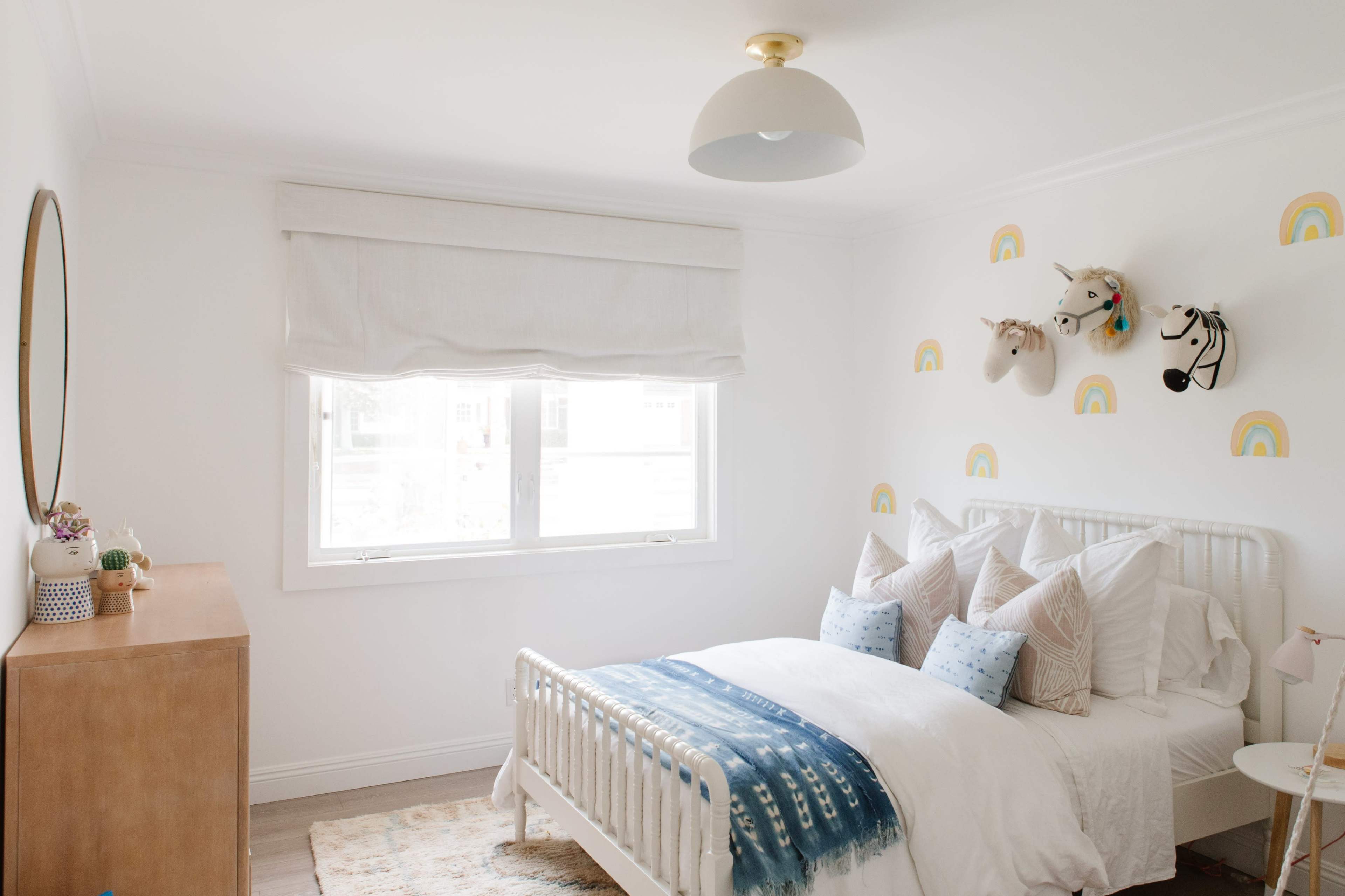 A neatly arranged bedroom features a white bed with decorative pillows, a wooden dresser, and whimsical unicorn wall decorations.
