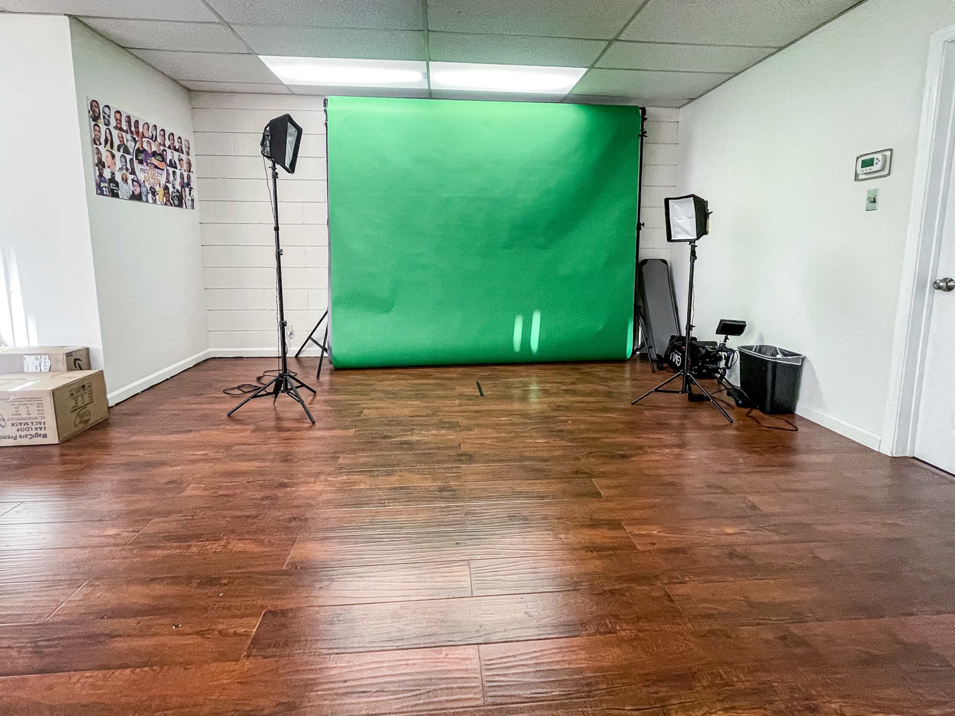 A room with a green screen backdrop, lighting equipment, and wooden flooring.