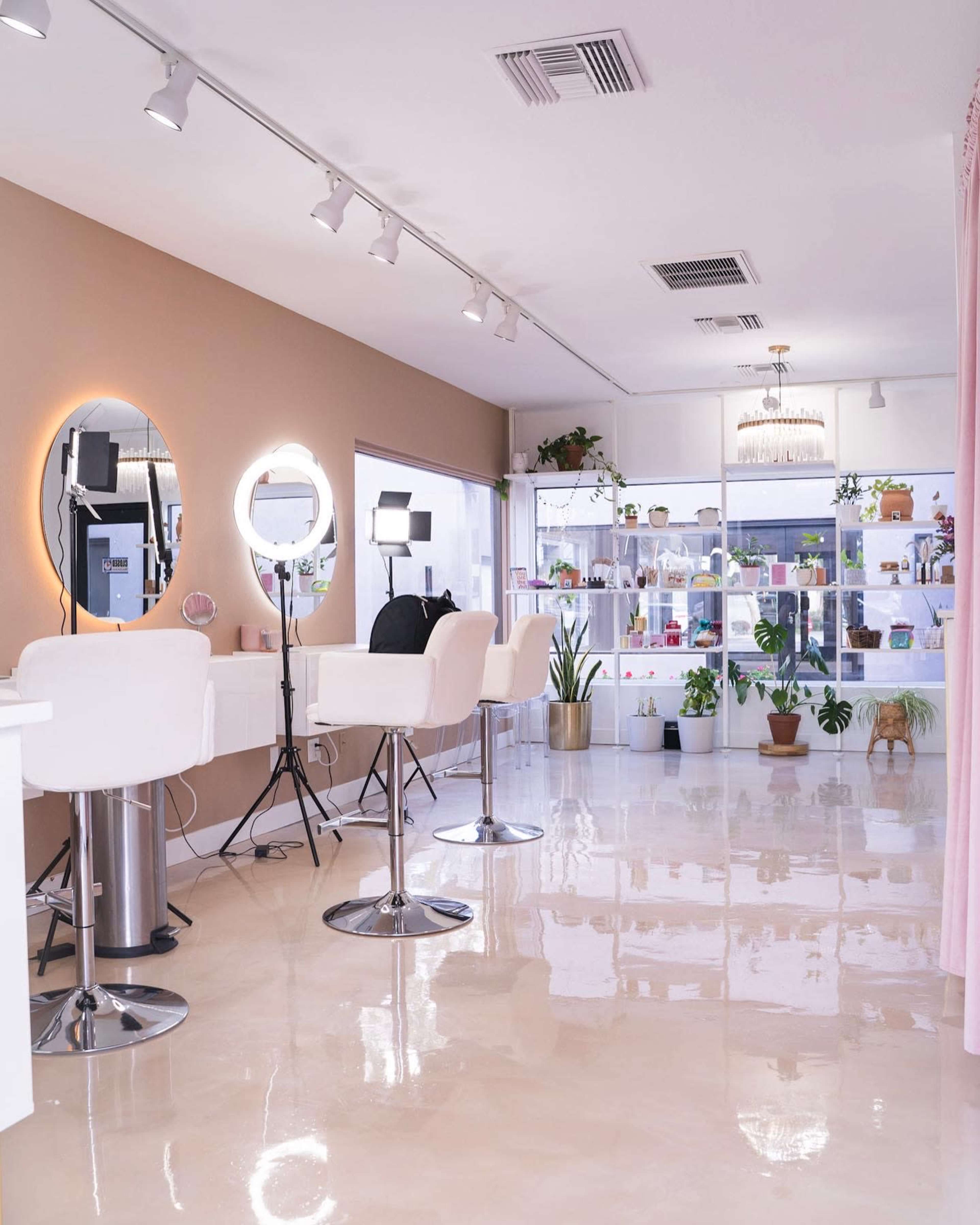 A modern beauty salon with white barstools, a large mirror, and various plants displayed in a brightly lit space.