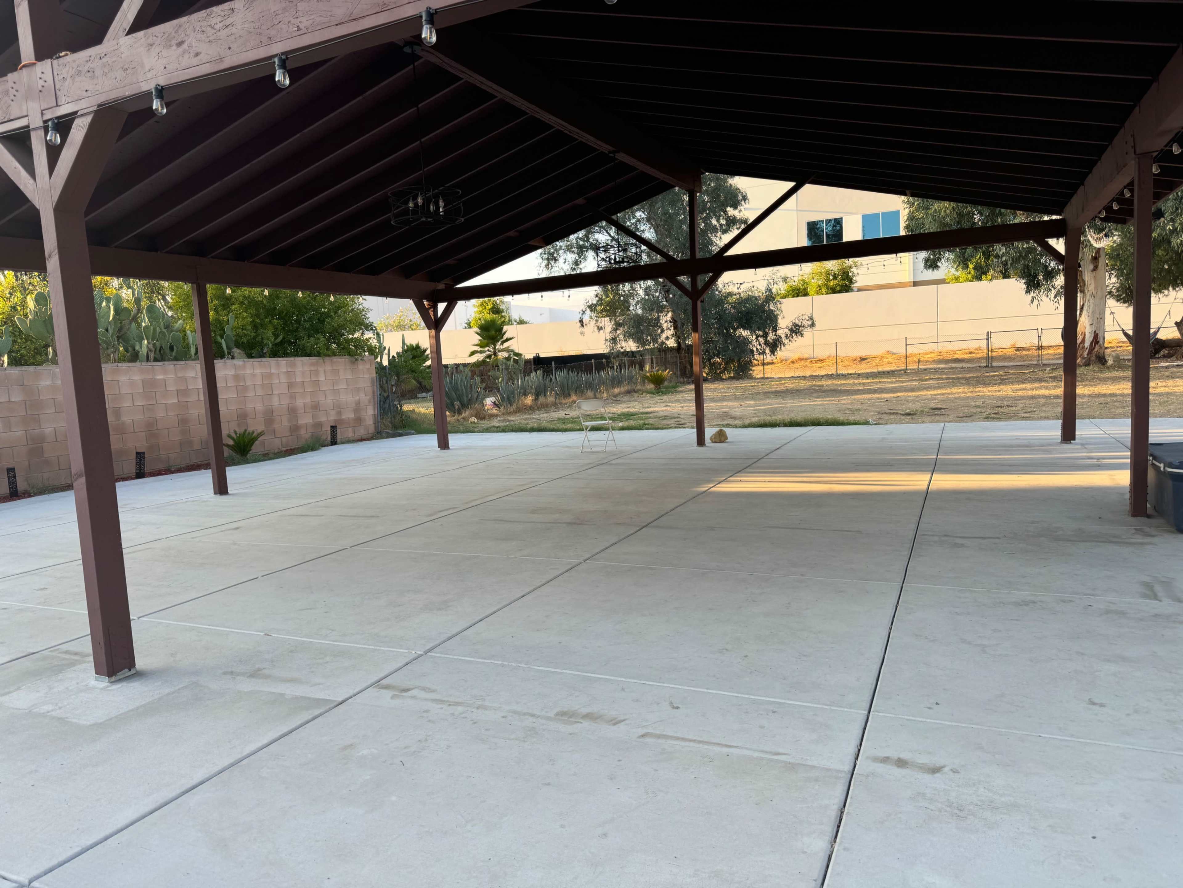 A spacious, uncovered concrete area is sheltered by a wooden pavilion with exposed beams.