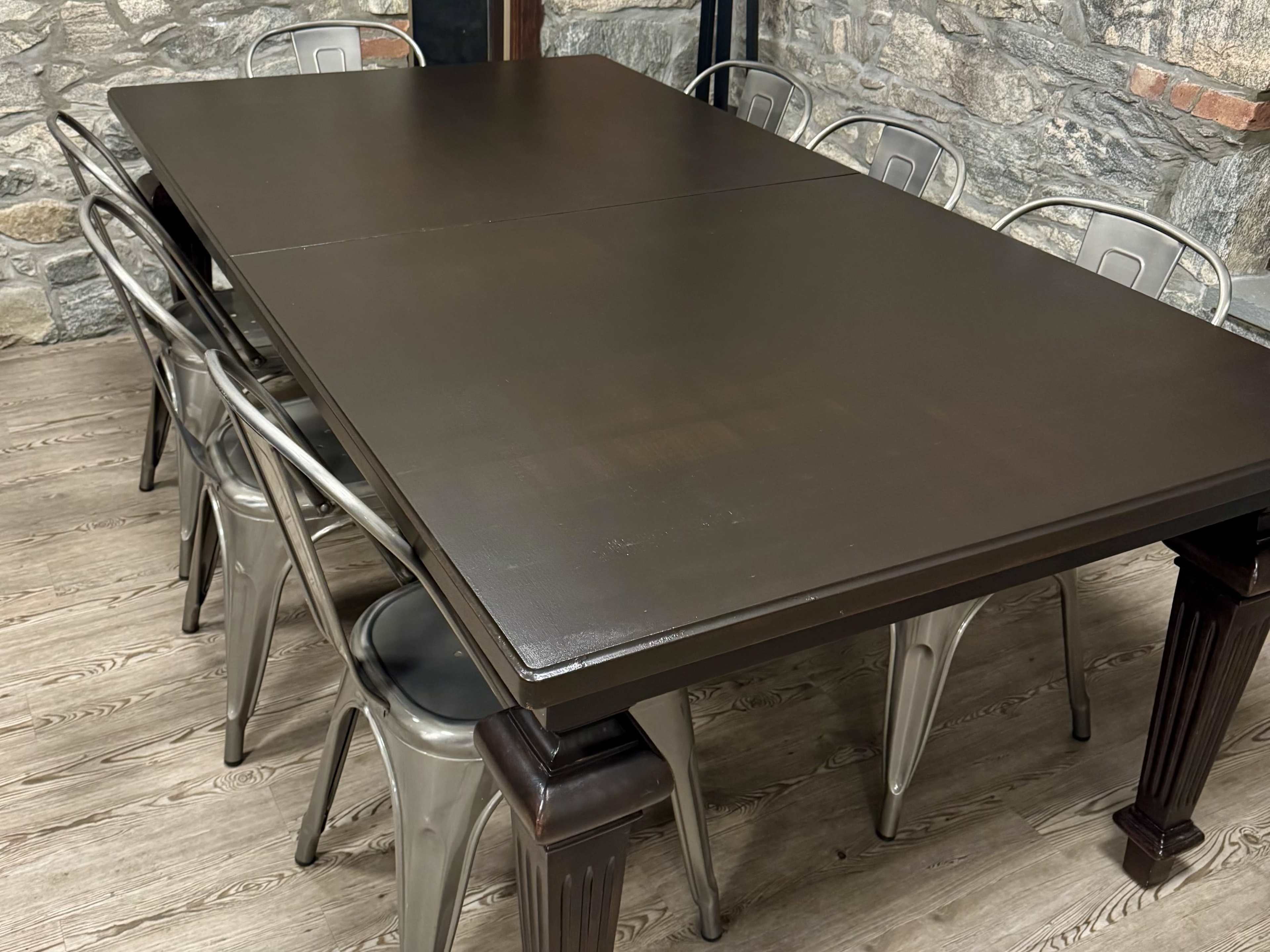 A large, dark wooden table is surrounded by metal chairs in a room with stone walls.