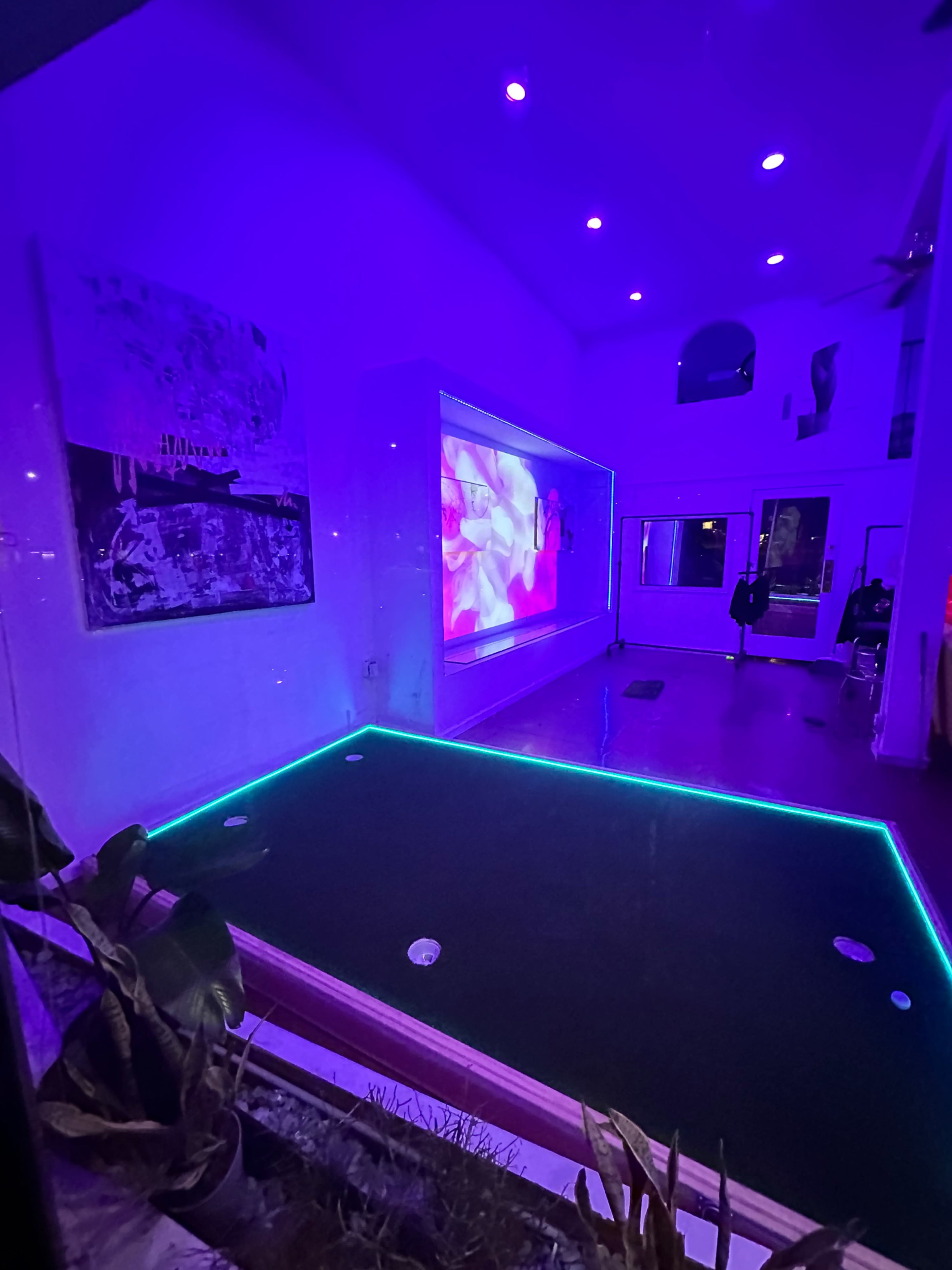 The image shows a dimly lit room with a glowing green putting green and vibrant purple lighting on the walls.