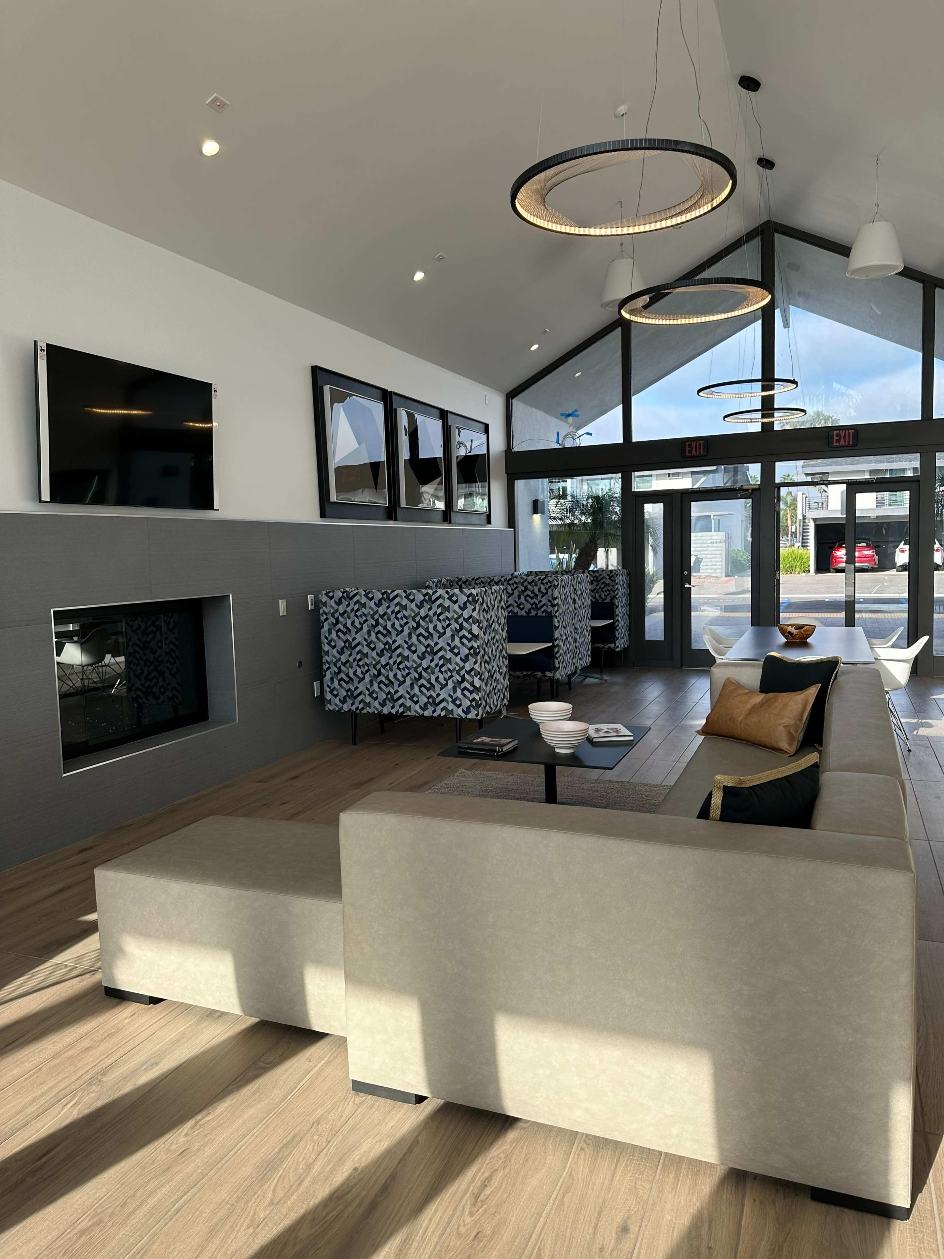 A modern lobby with a large sectional sofa, decorative light fixtures, and a fireplace, featuring seating areas separated by patterned dividers.